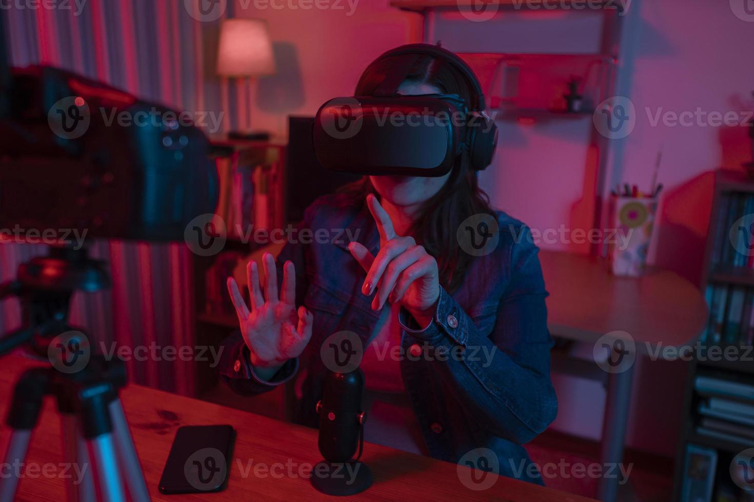 hermosa mujer hispana frente a una cámara de video grabando un blog en su estudio con luces rojas y azules dentro de su casa foto