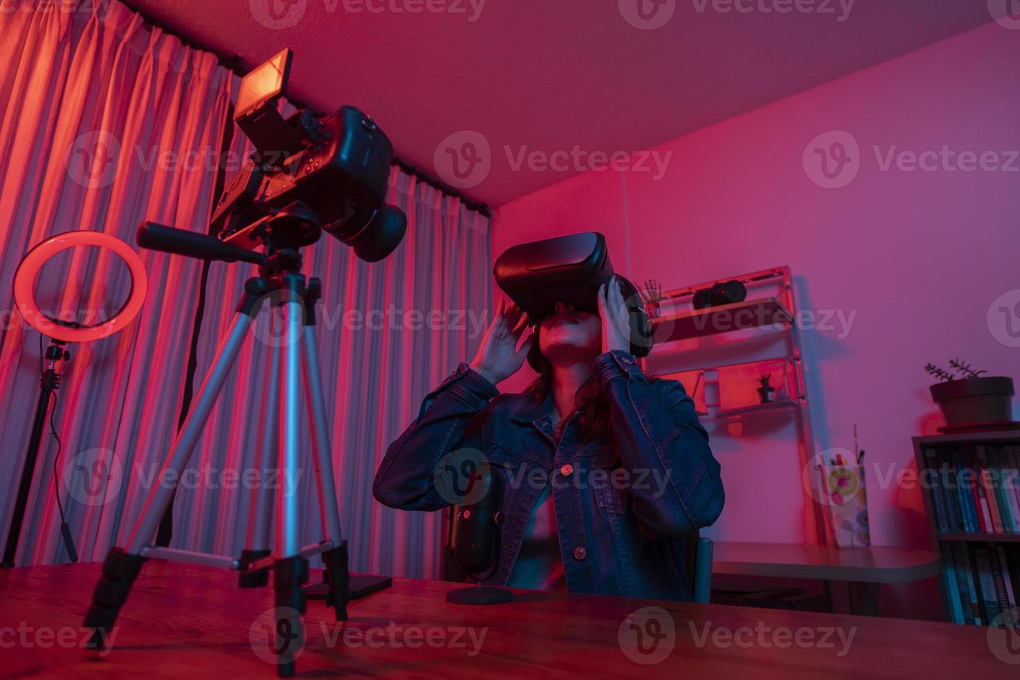 Beautiful Hispanic woman in front of a video camera recording a blog in her studio with red and blue lights inside her house photo