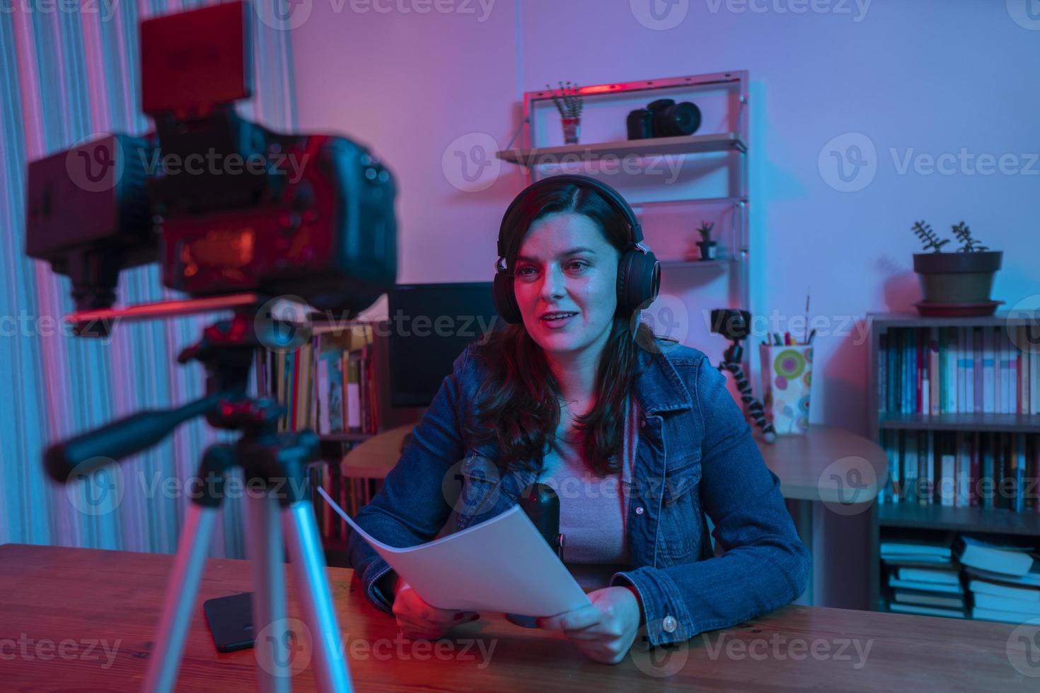 hermosa mujer hispana frente a una cámara de video grabando un blog en su estudio con luces rojas y azules dentro de su casa foto