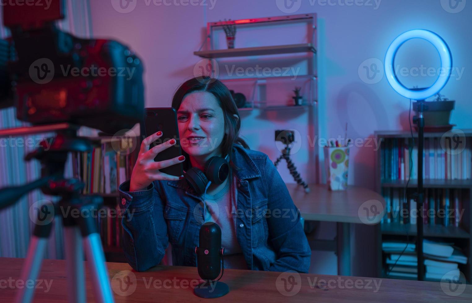 Beautiful Hispanic woman in front of a video camera recording a blog in her studio with red and blue lights inside her house photo
