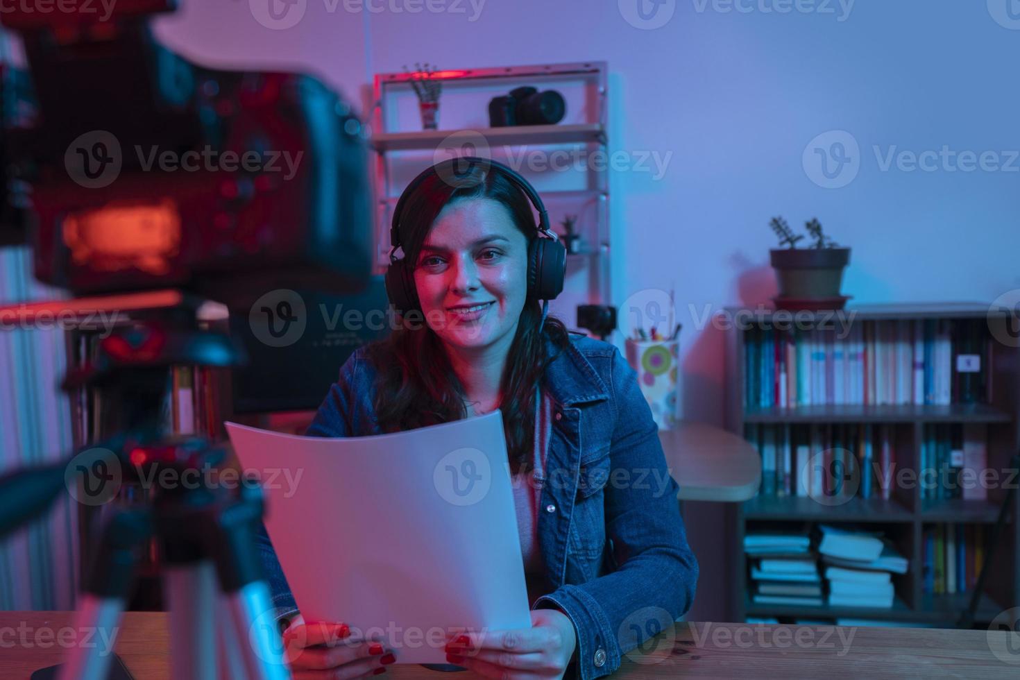 hermosa mujer hispana frente a una cámara de video grabando un blog en su estudio con luces rojas y azules dentro de su casa foto