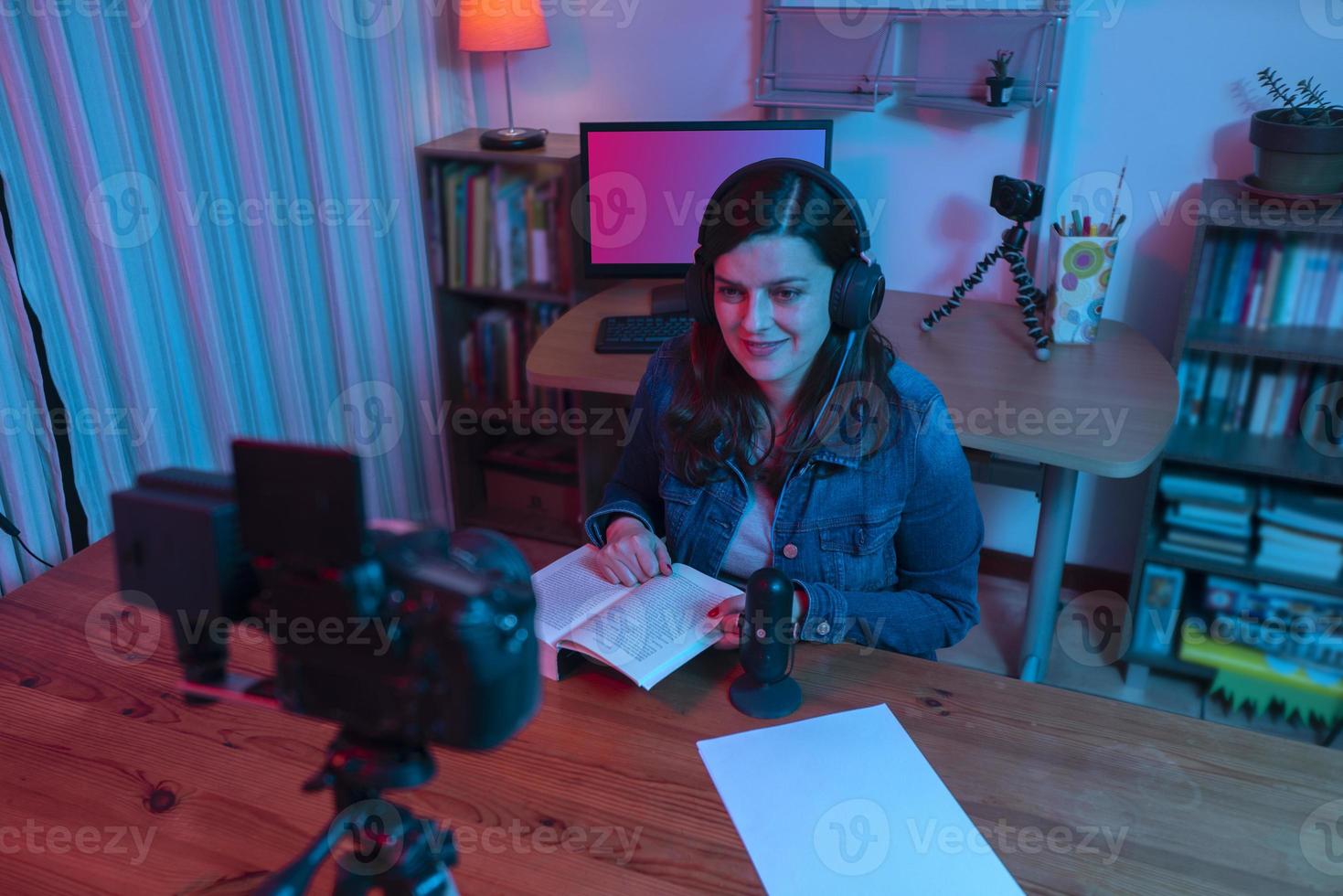 hermosa mujer hispana frente a una cámara de video grabando un blog en su estudio con luces rojas y azules dentro de su casa foto