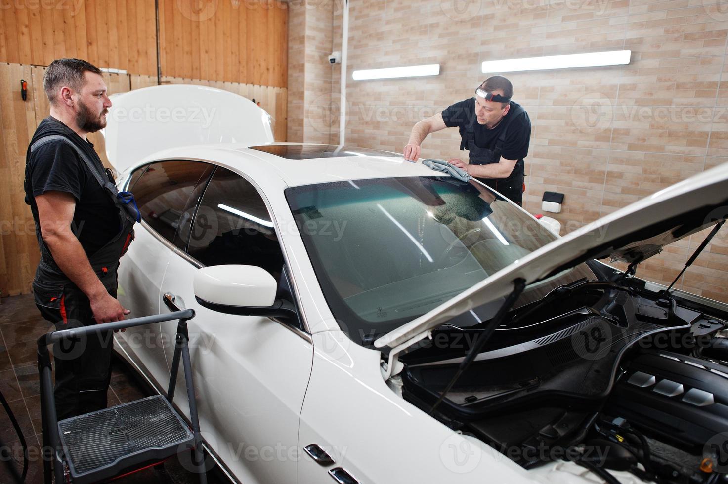 Worker in detailing garage put polyurethane anti-gravel film cover in white luxury car. photo