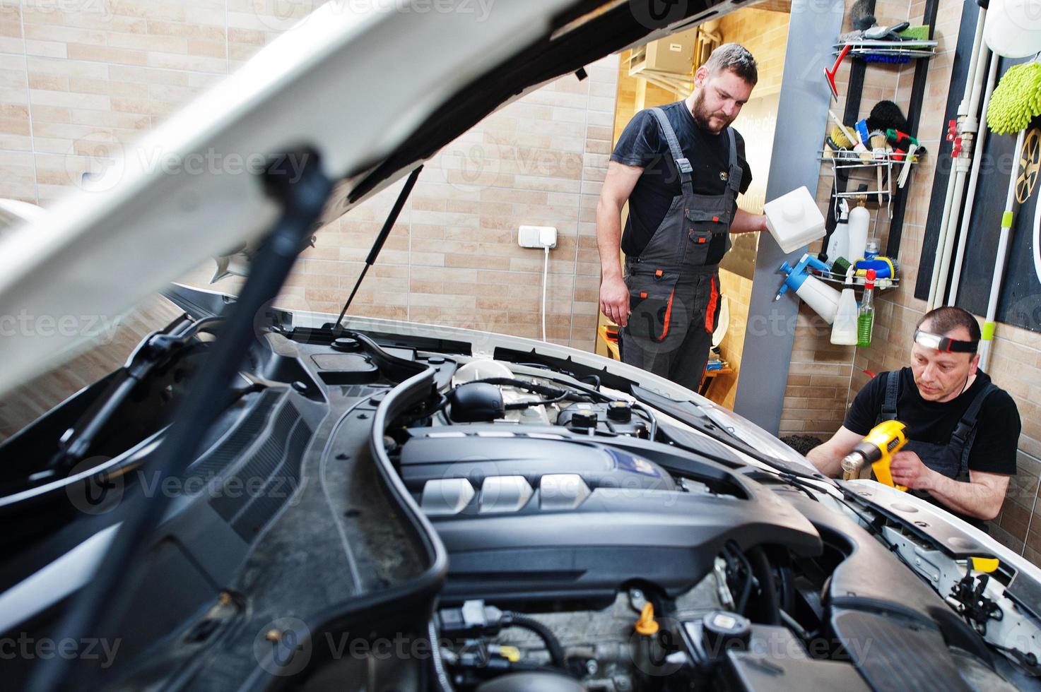 Worker in detailing garage put polyurethane anti-gravel film cover in white luxury car. photo