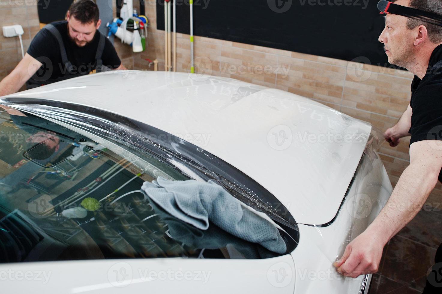 Worker in detailing garage put polyurethane anti-gravel film cover in white luxury car. photo