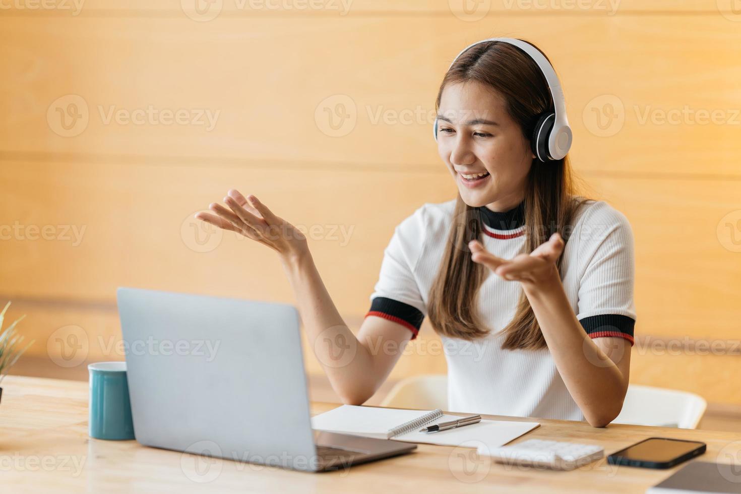 Smiling Asian young female using headset looking at laptop screen listen and learning online courses. Happy chinese business woman with headphones video call for customer service photo