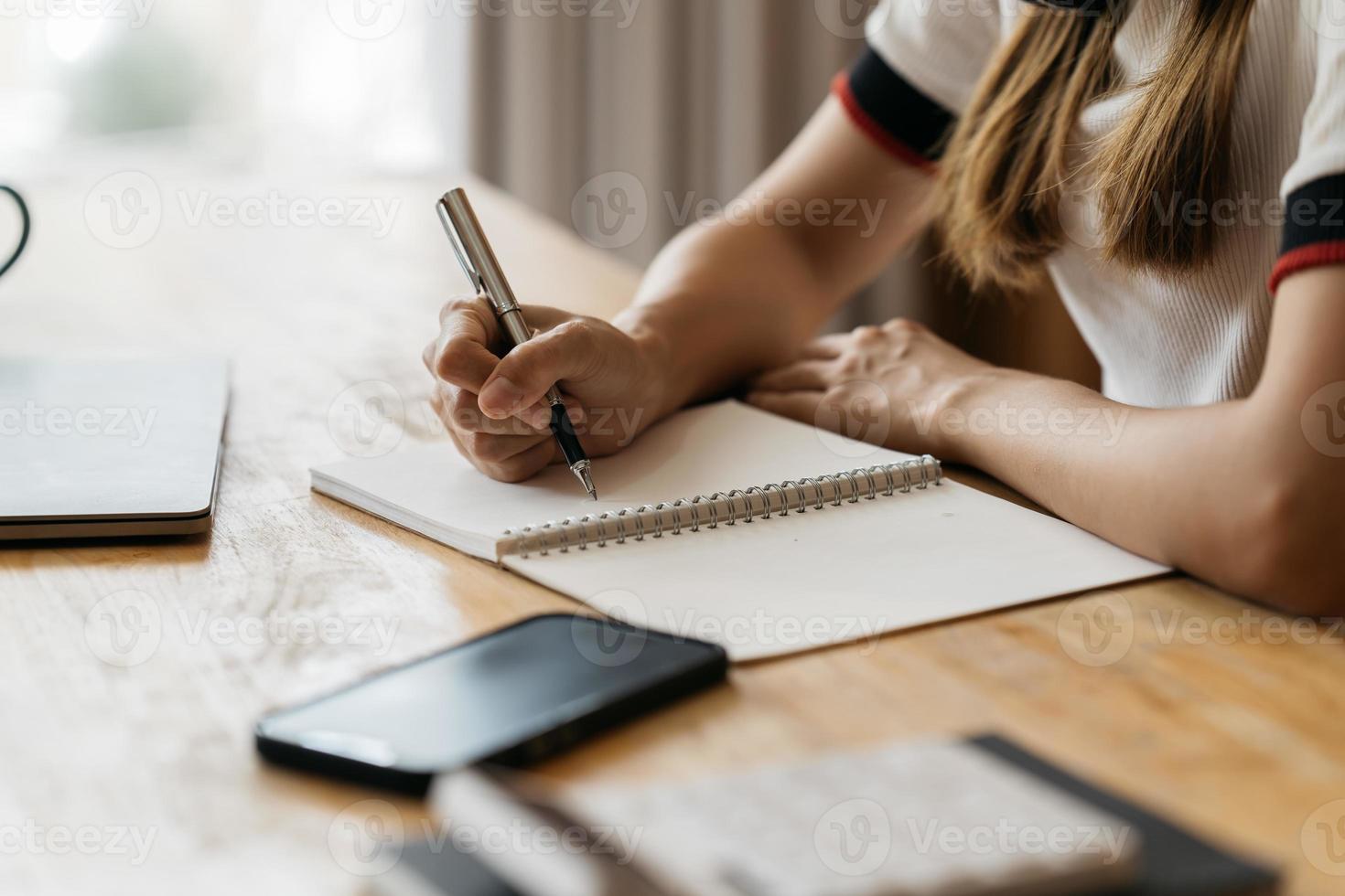 Close up of student girl hand writing on notebook on a desk at home. photo