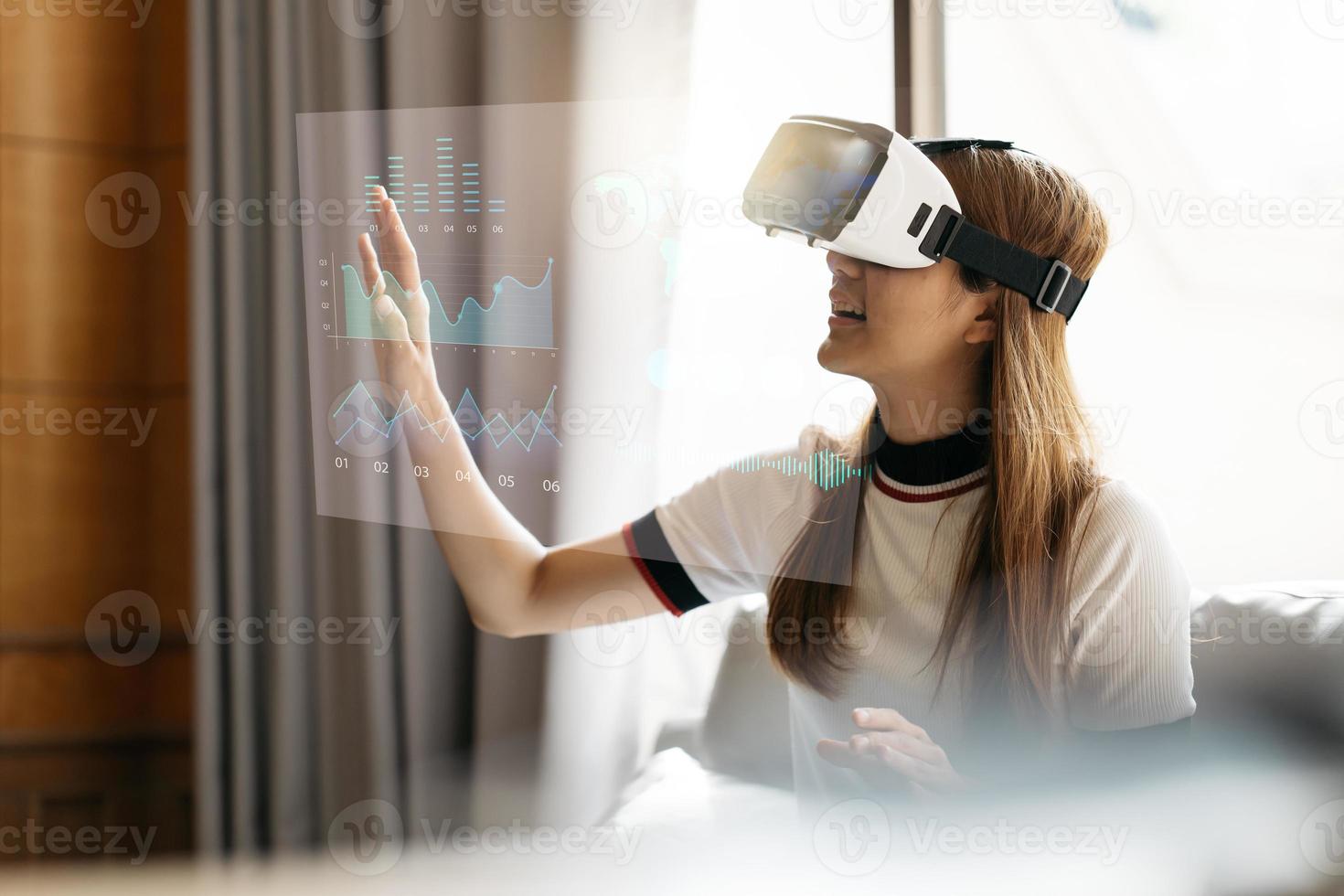 Conceptual image of confident and successful business woman in suit sitting inside office building with financial interface and using virtual reality headset. photo