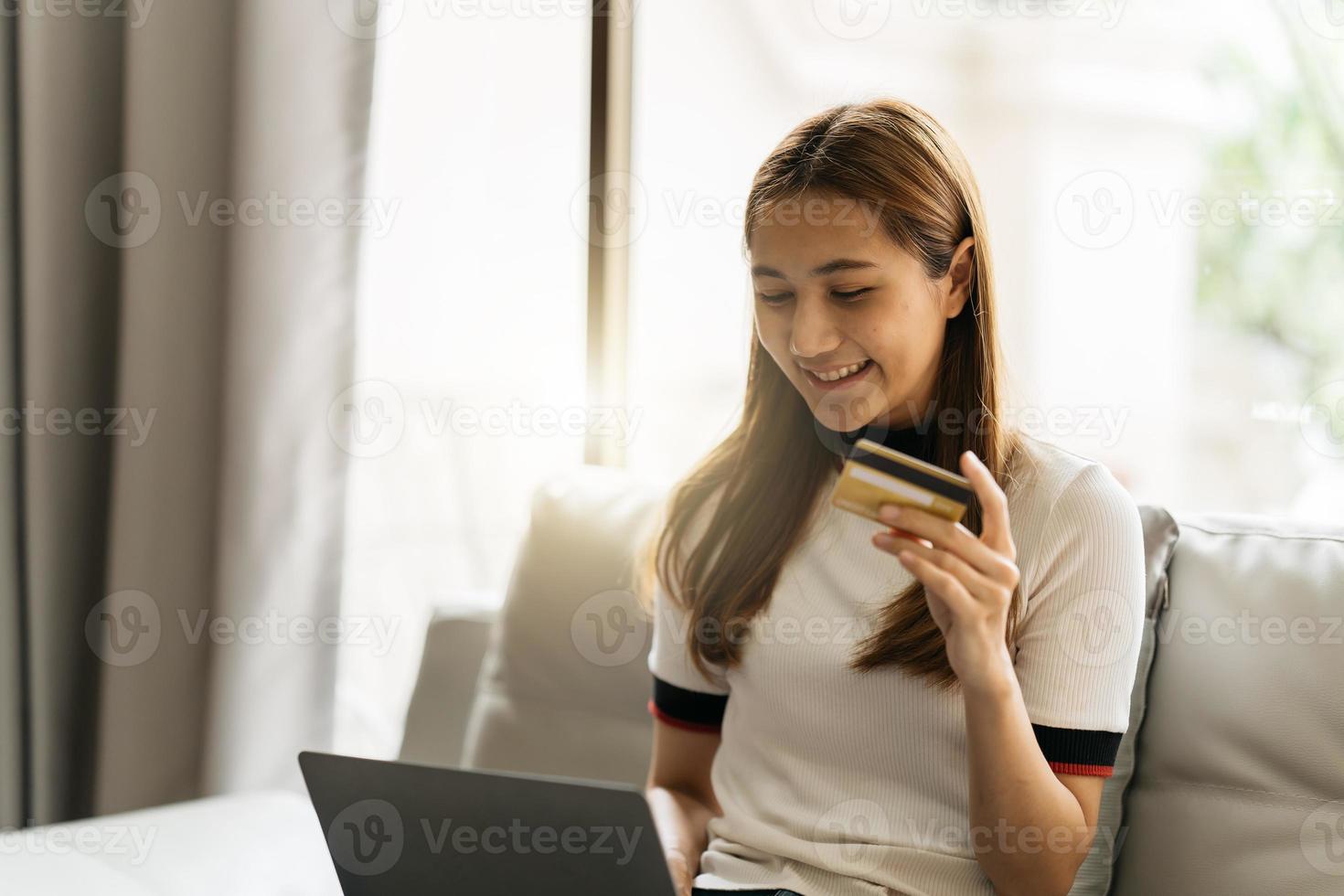 concepto de compras en línea. mujer asiática soñadora con computadora portátil y tarjeta de crédito sentada en el sofá, pensando en compras por Internet o entrega de alimentos, espacio libre. foto