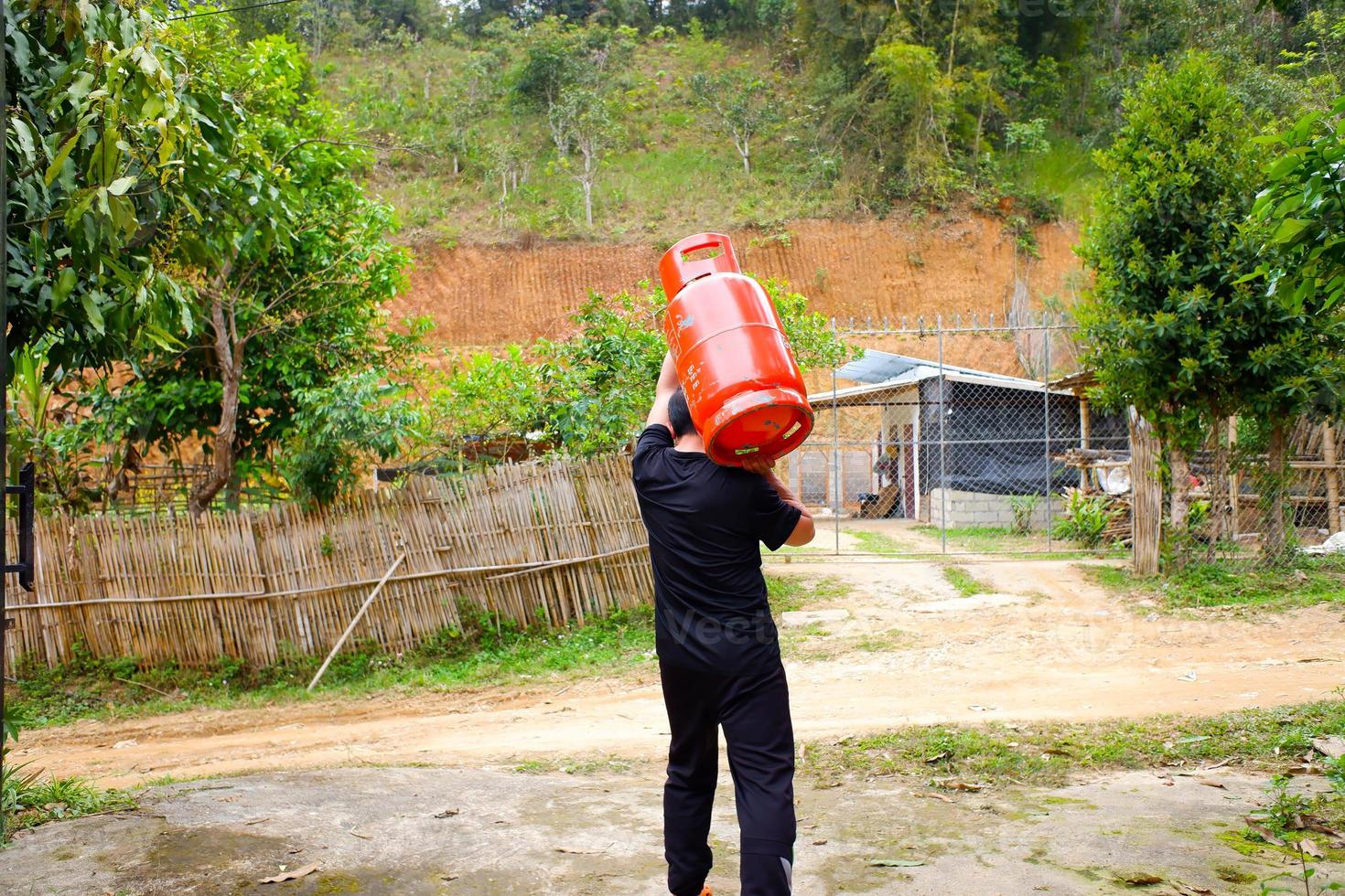 A man wearing a gas cylinder on his shoulder. Men wearing an orange tank gas. photo