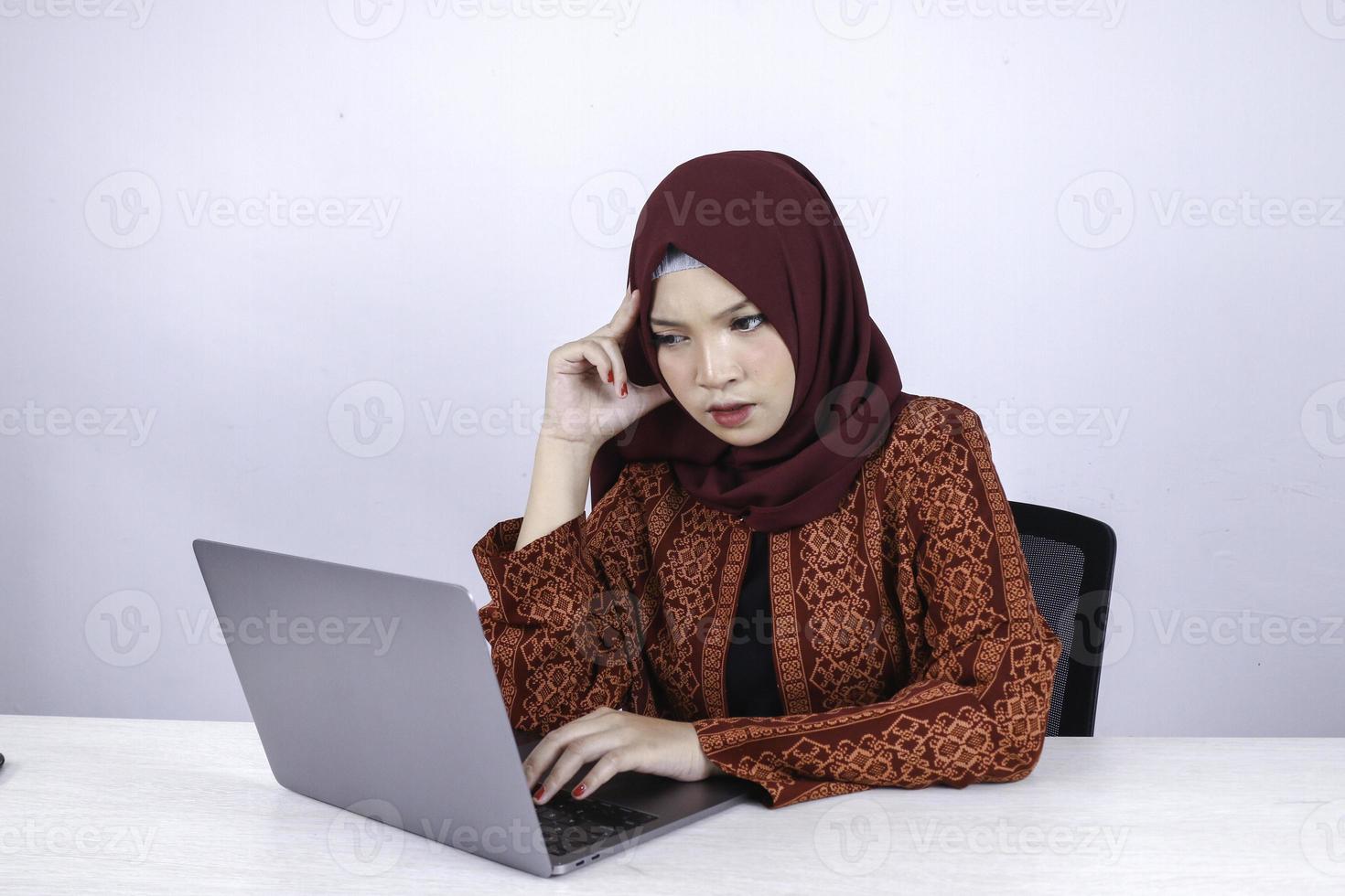 Young Asian Islam woman is serious look with thinking gesture hand on face on the front of Laptop. photo