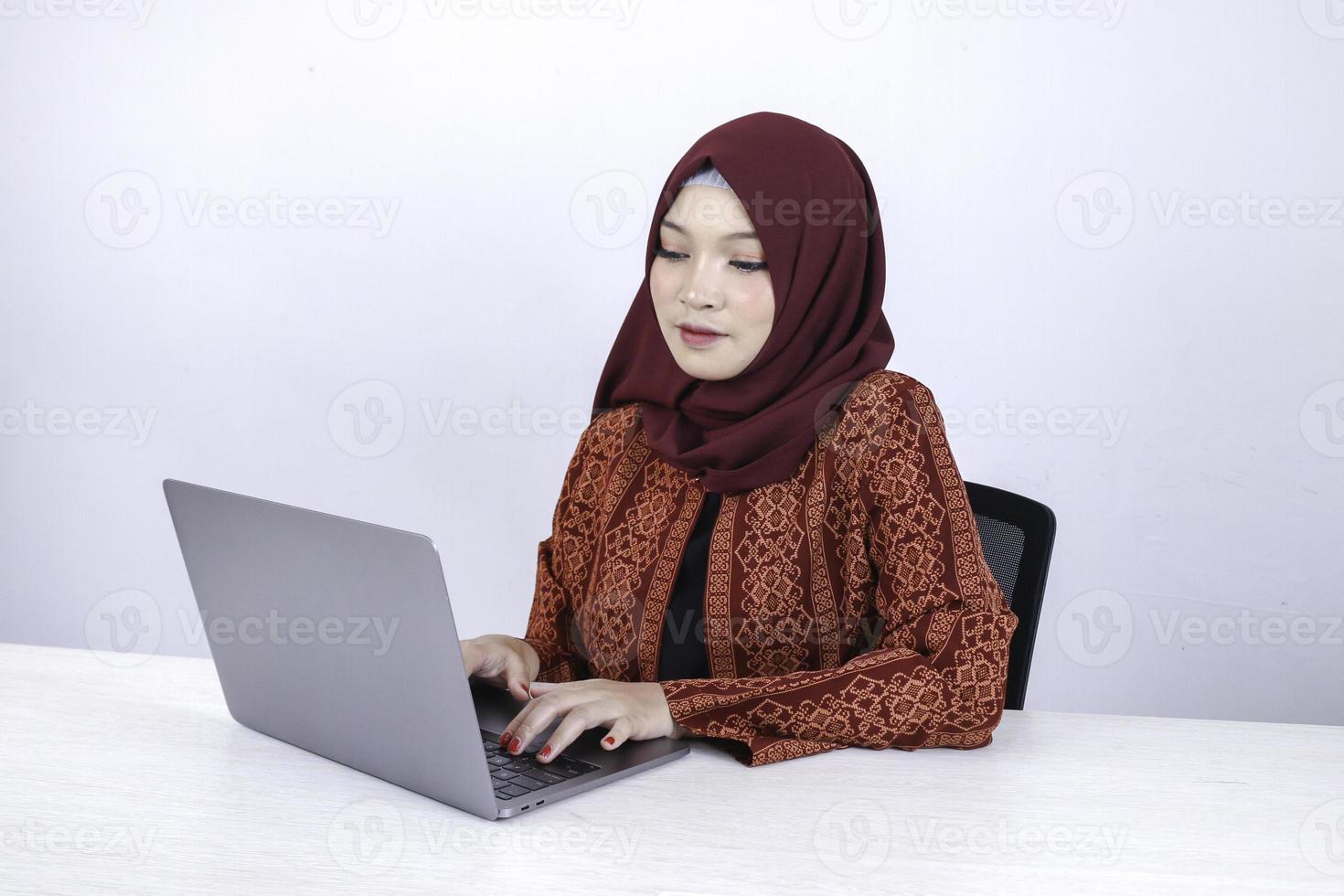 Young Asian Islam woman is sitting enjoy and smiling when working on laptop on white background. photo
