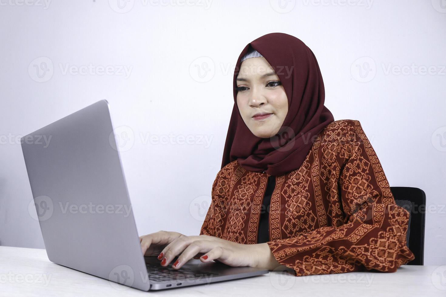 Young Asian Islam woman is serious look with thinking gesture hand on face on the front of Laptop. photo