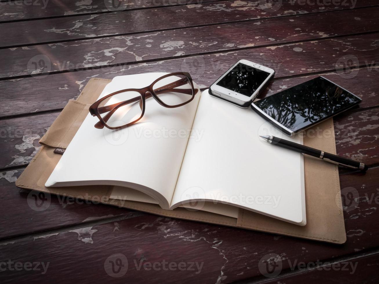 Workspace with glasses, pen and smartphone, note paper and notebook on old wooden table photo