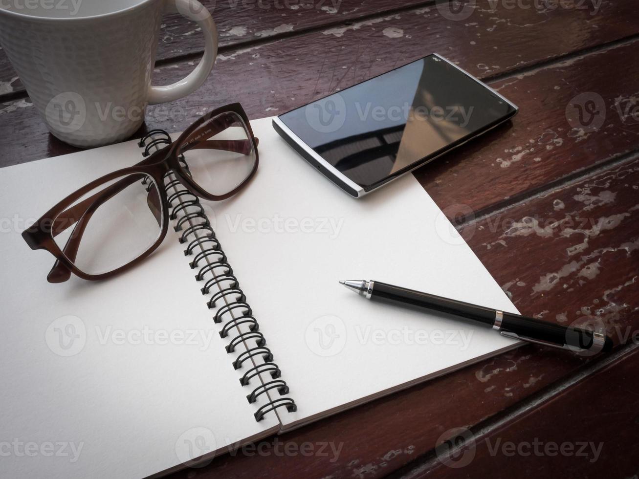 Workspace with glasses, pen, smartphone and coffee cup, note paper and notebook on old wooden table photo