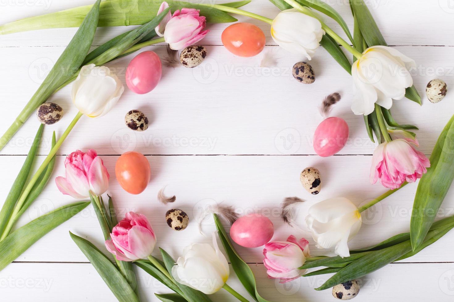 Beautiful pink tulips with colorful quail and chicken eggs in nest on white wooden background. Spring and Easter holiday concept with copy space. photo
