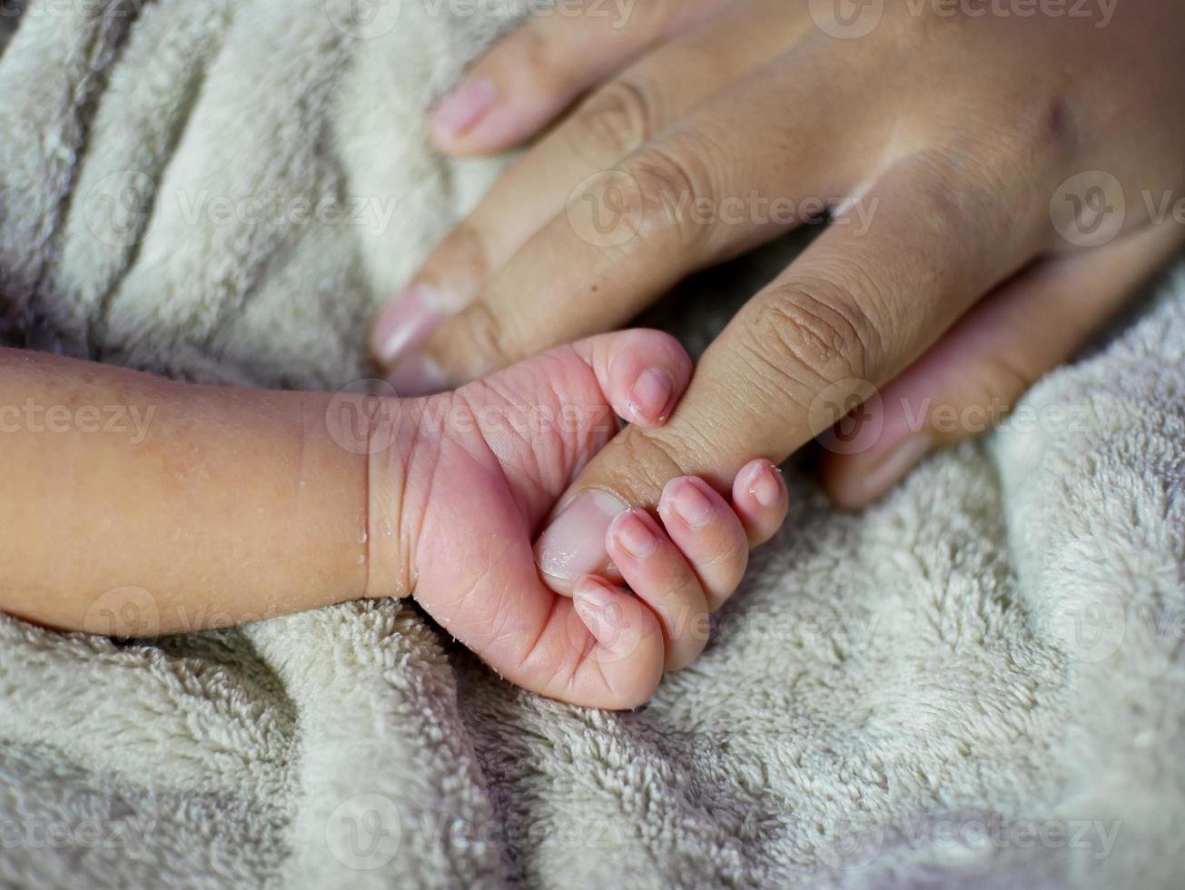 Newborn baby grasping her mother's finger. Concept of baby care, feeling safe, parent love. Selective soft focus. photo