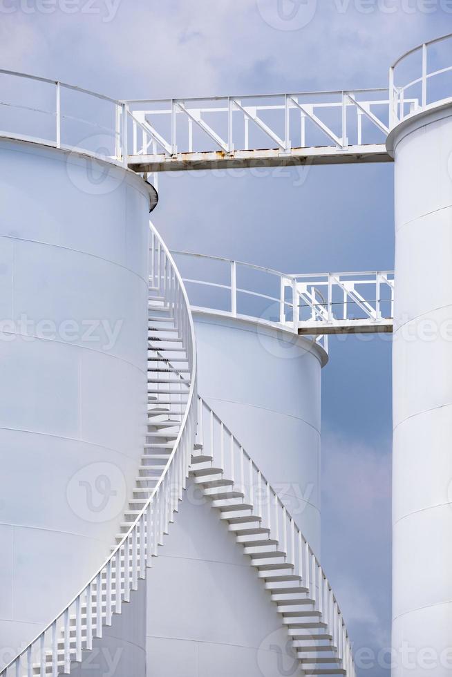 Low angle view of curve spiral staircase on white storage fuel tanks in vertical frame photo