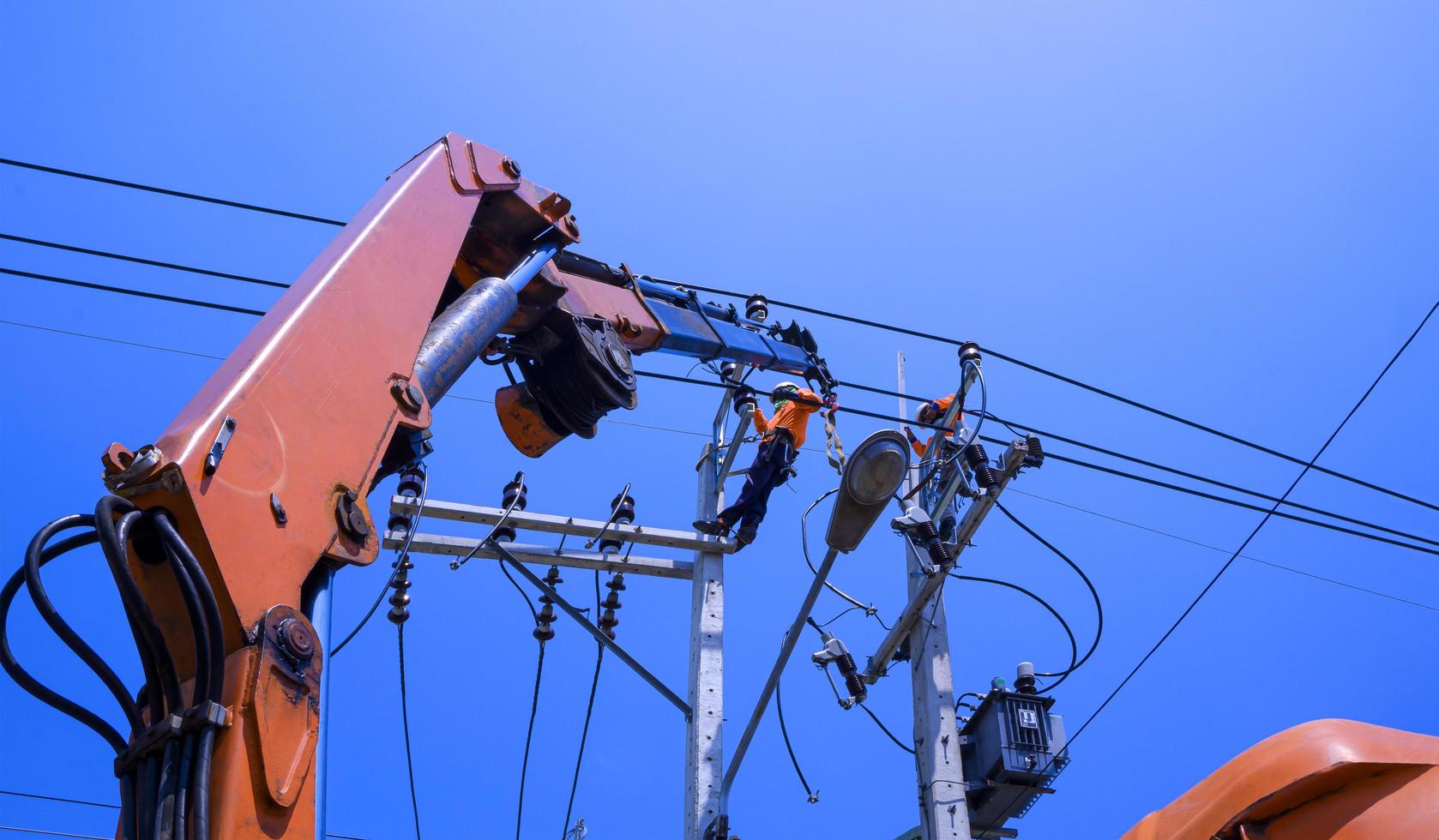 vista de ángulo bajo de dos electricistas con camión grúa están trabajando para instalar transmisión eléctrica en postes de energía eléctrica contra fondo de cielo azul claro foto