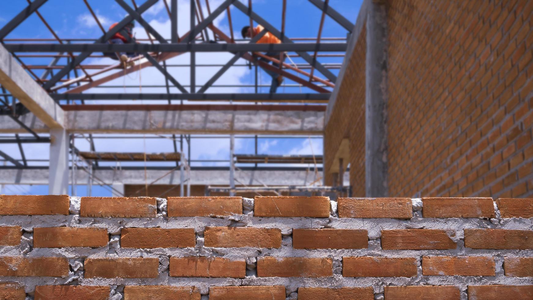 Focus at brick wall with blurred background of 2 builder workers are working on roof structure in house construction site photo