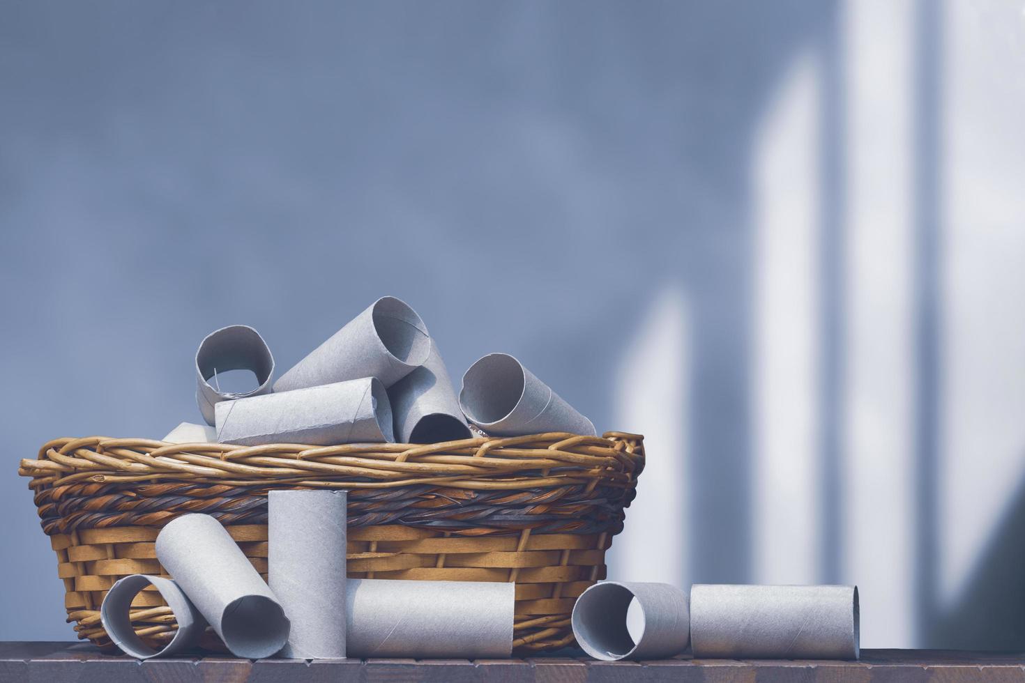 A lot of empty tissue roll cores in wicker basket on wooden table with blurred loft cement wall background, paper recycling and reuse concept photo