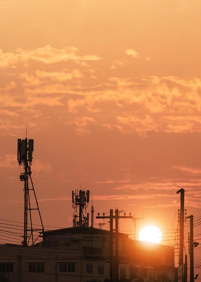 Silhouette of Telecommunication tower with antennas on top of building against sunset sky background in vertical frame photo
