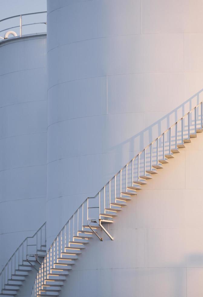Morning sunshine on curve spiral staircase surface of white storage fuel tanks in vertical frame photo