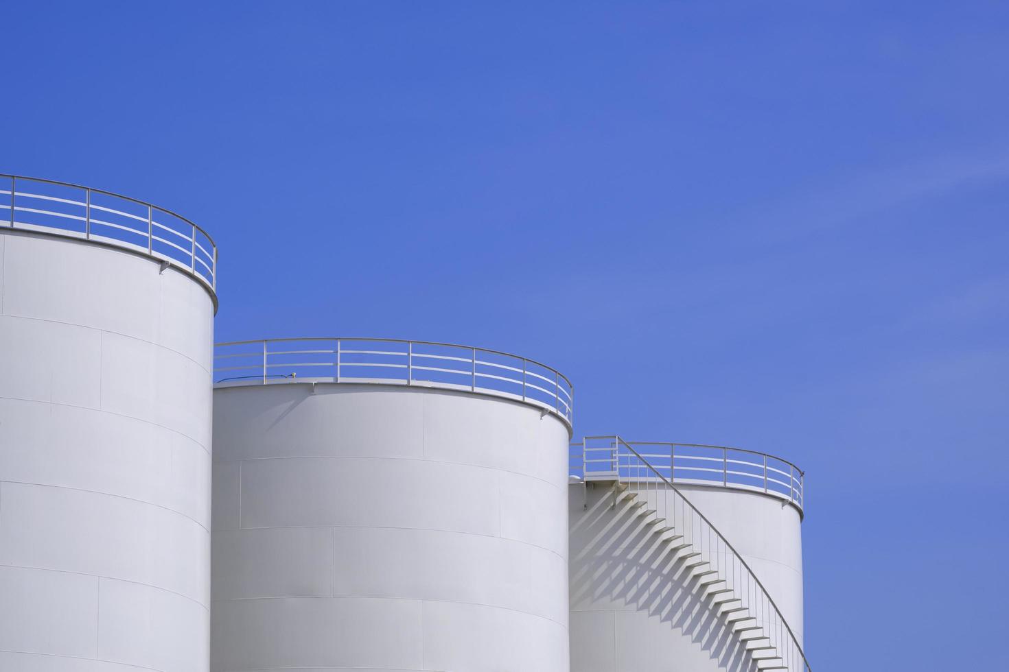 Three white oil storage fuel tanks against blue sky background, low angle view with copy space photo