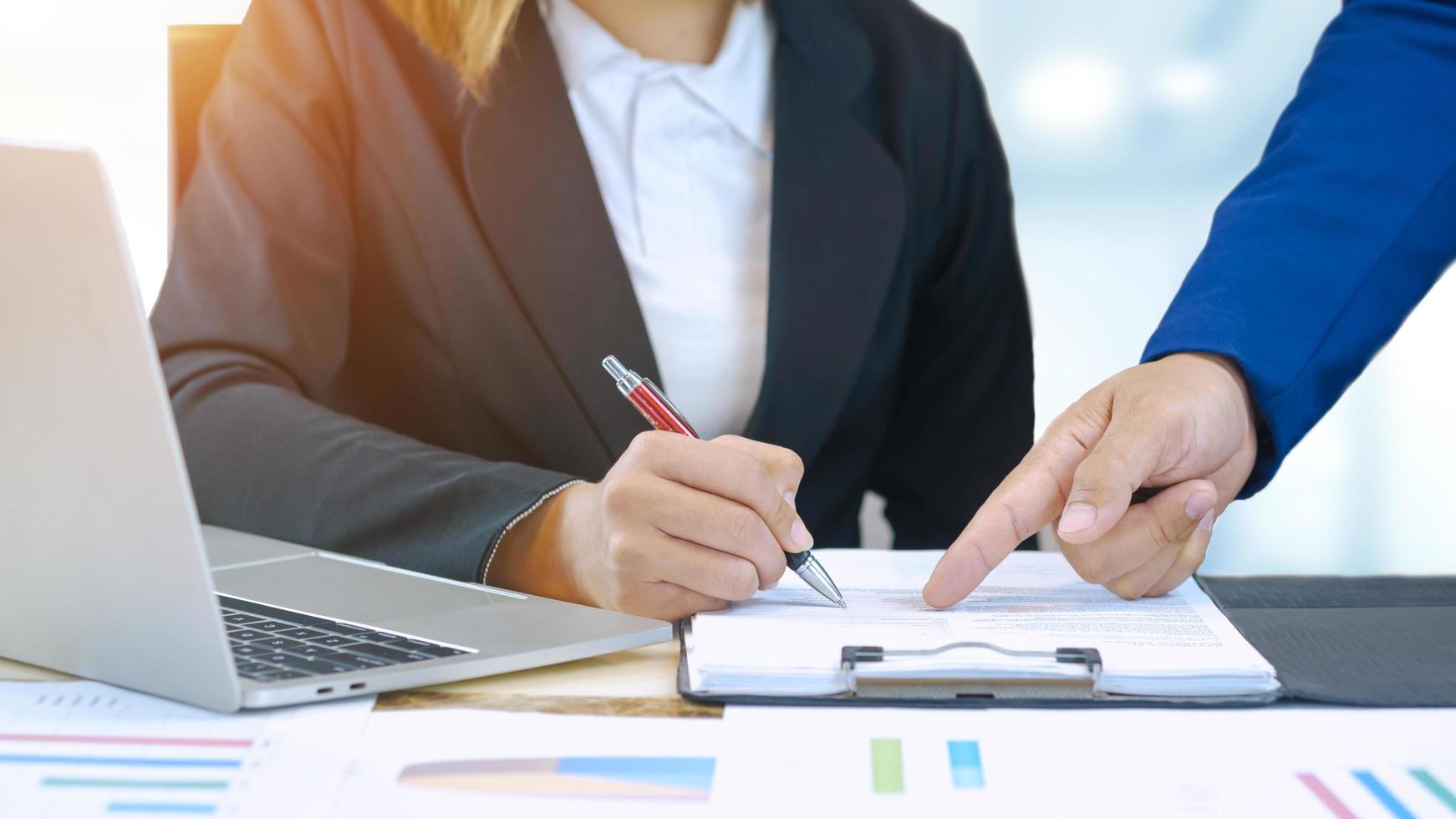 Focus at businessman's hand is pointing at paperwork on female staff's desk during company development system planning in office room photo