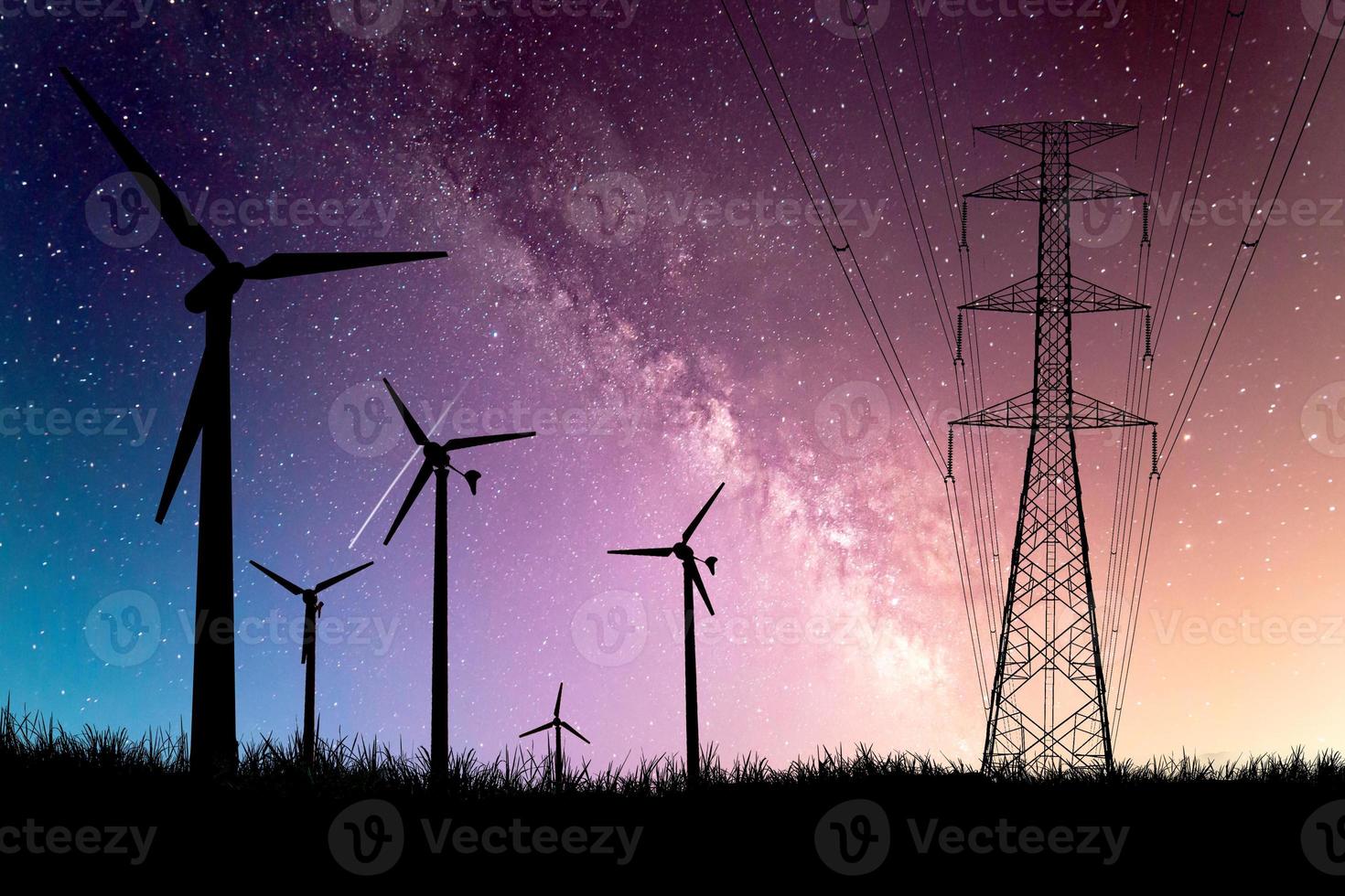 A silhouette of a windmill used to generate electricity in a field against a beautiful Milky Way backdrop. photo