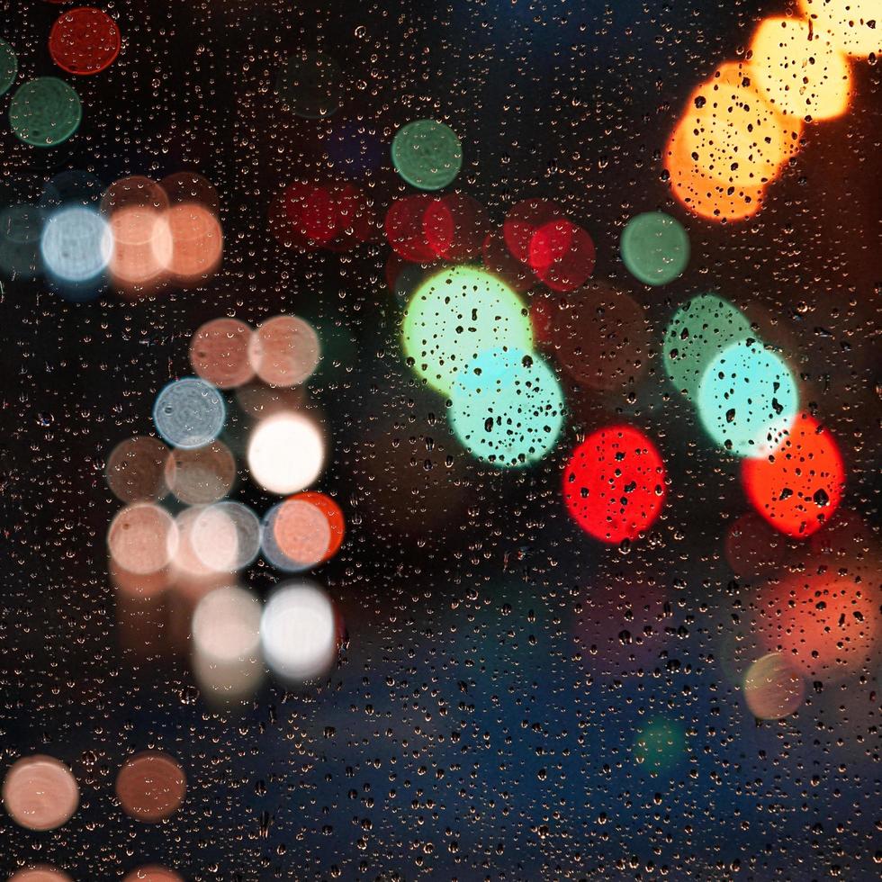 gotas de lluvia en la ventana y luces de la calle por la noche en la ciudad foto