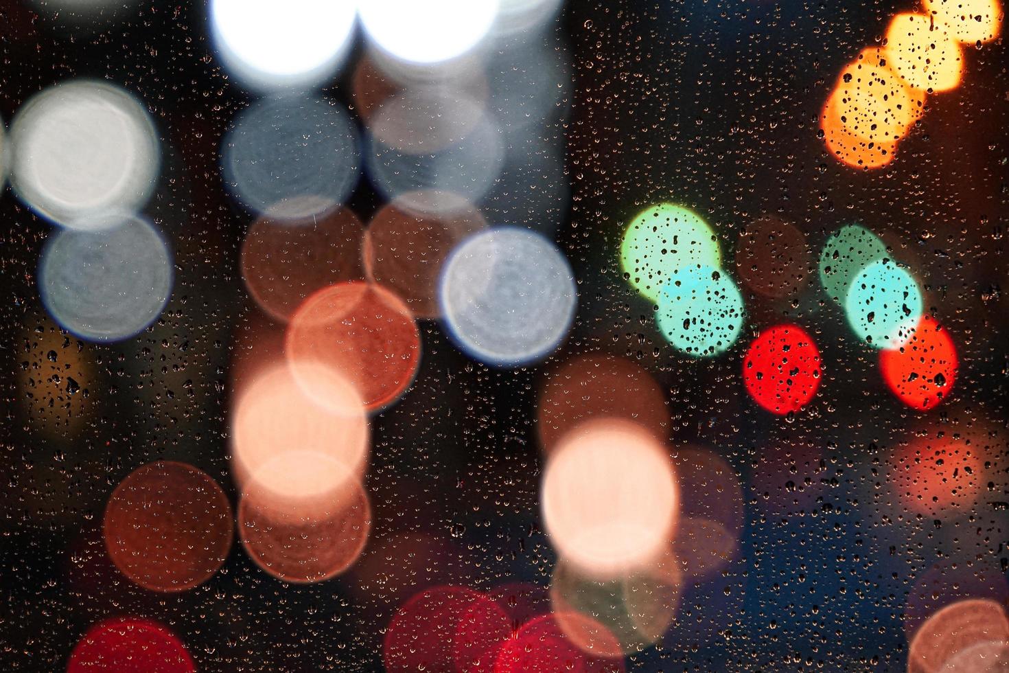 gotas de lluvia en la ventana y luces de la calle por la noche en la ciudad foto