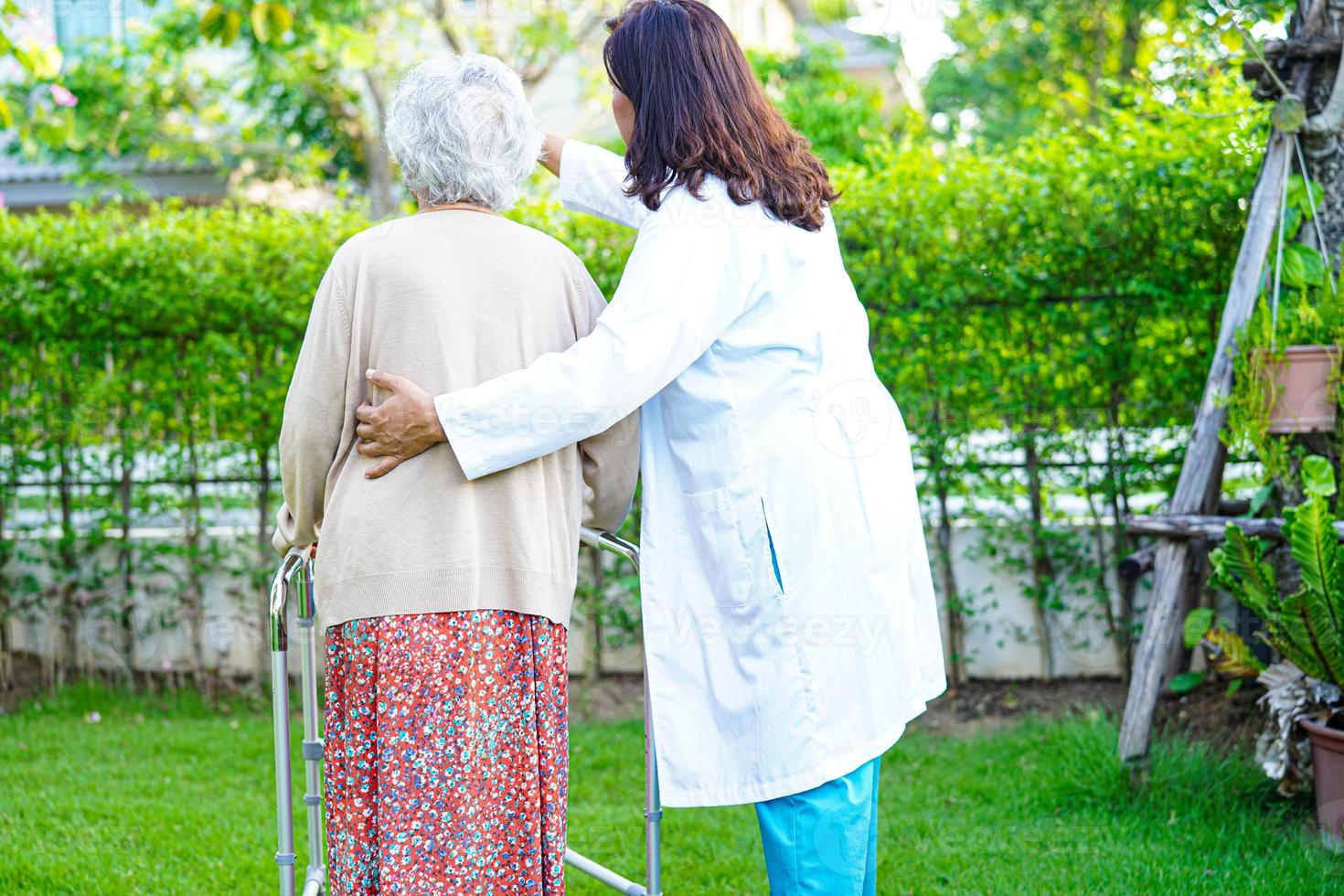 el médico ayuda a una anciana asiática con discapacidad a caminar con un andador en el parque, concepto médico. foto