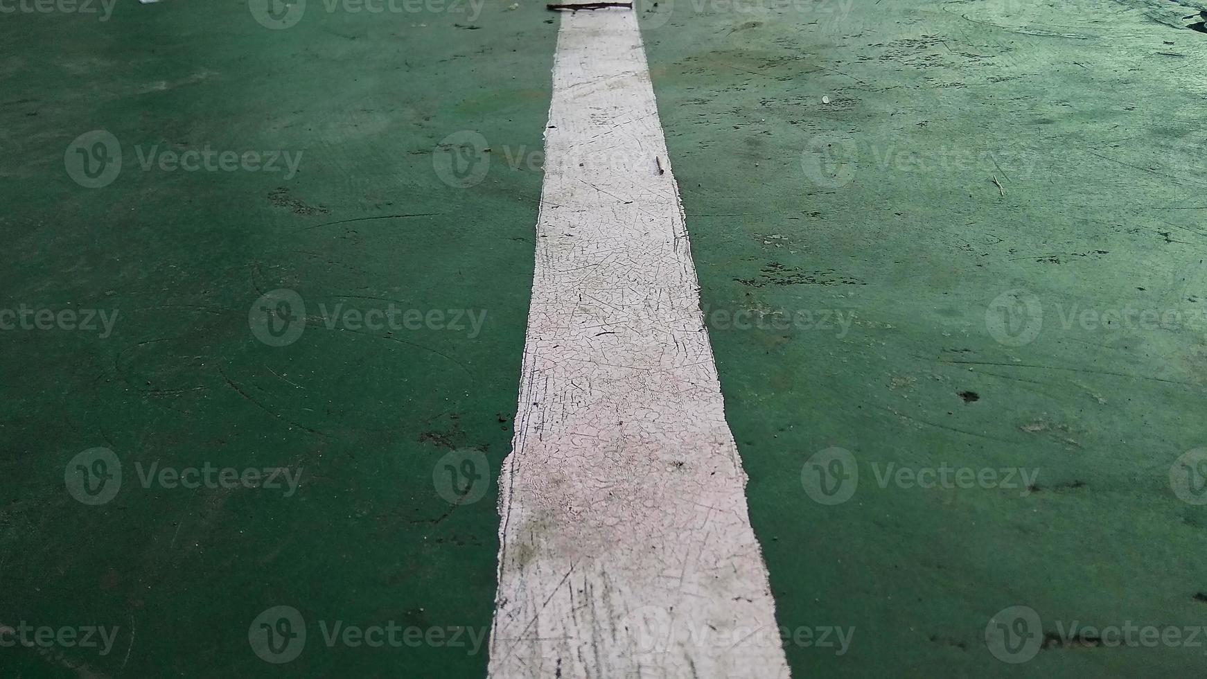 Close up of a chapped-white line drawn on a green-broken floor at public sports field. photo