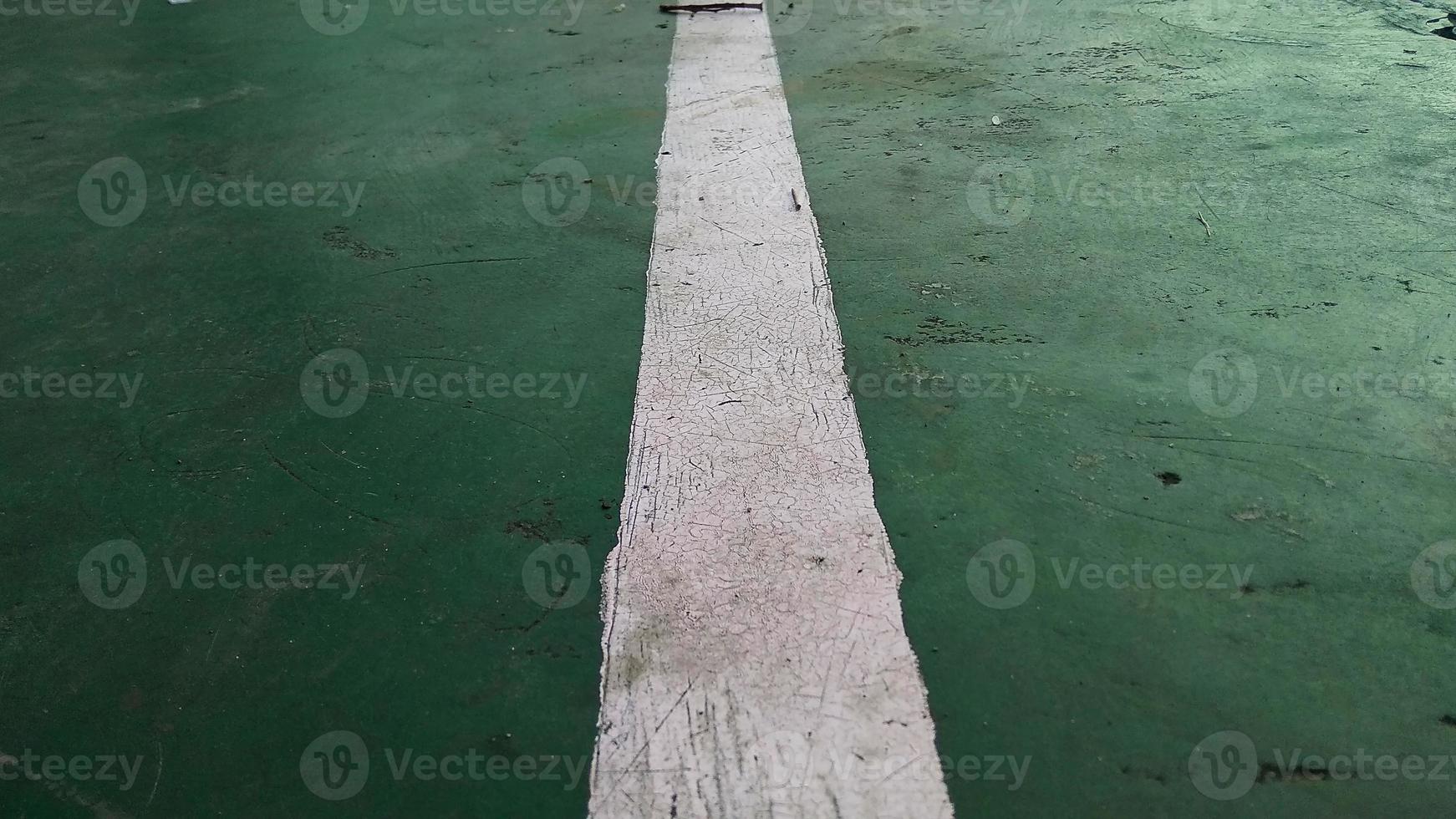 Close up of a chapped-white line drawn on a green-broken floor at public sports field. photo