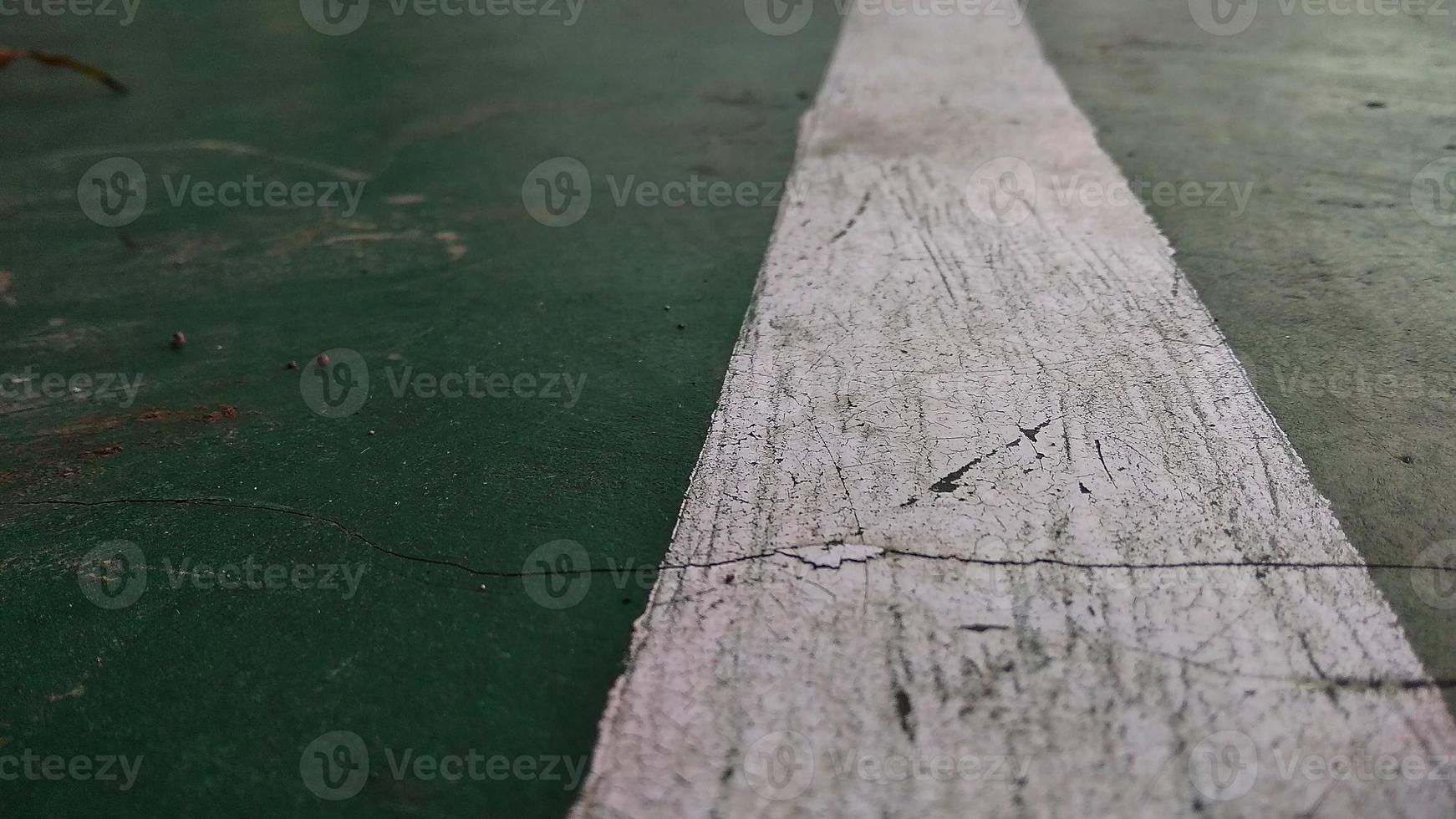 Close up of a chapped-white line drawn on a green-broken floor at public sports field. photo
