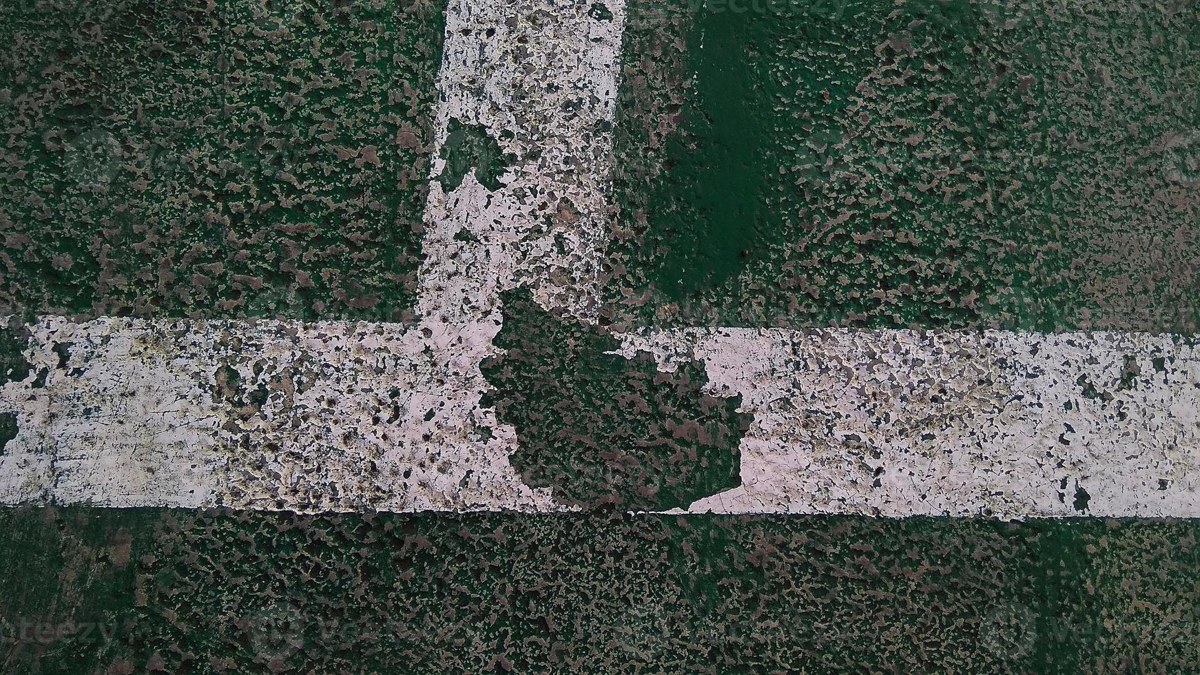 Close up of a chapped-white line drawn on a green-broken floor at public sports field. photo