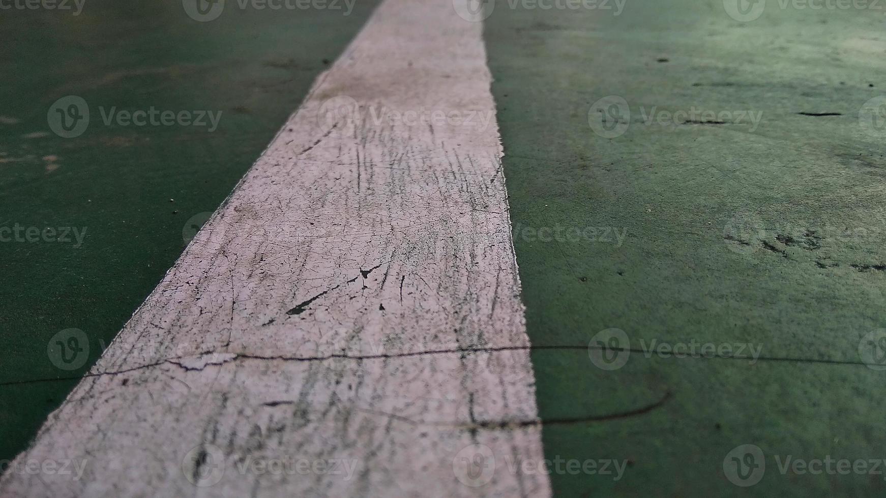 Close up of a chapped-white line drawn on a green-broken floor at public sports field. photo