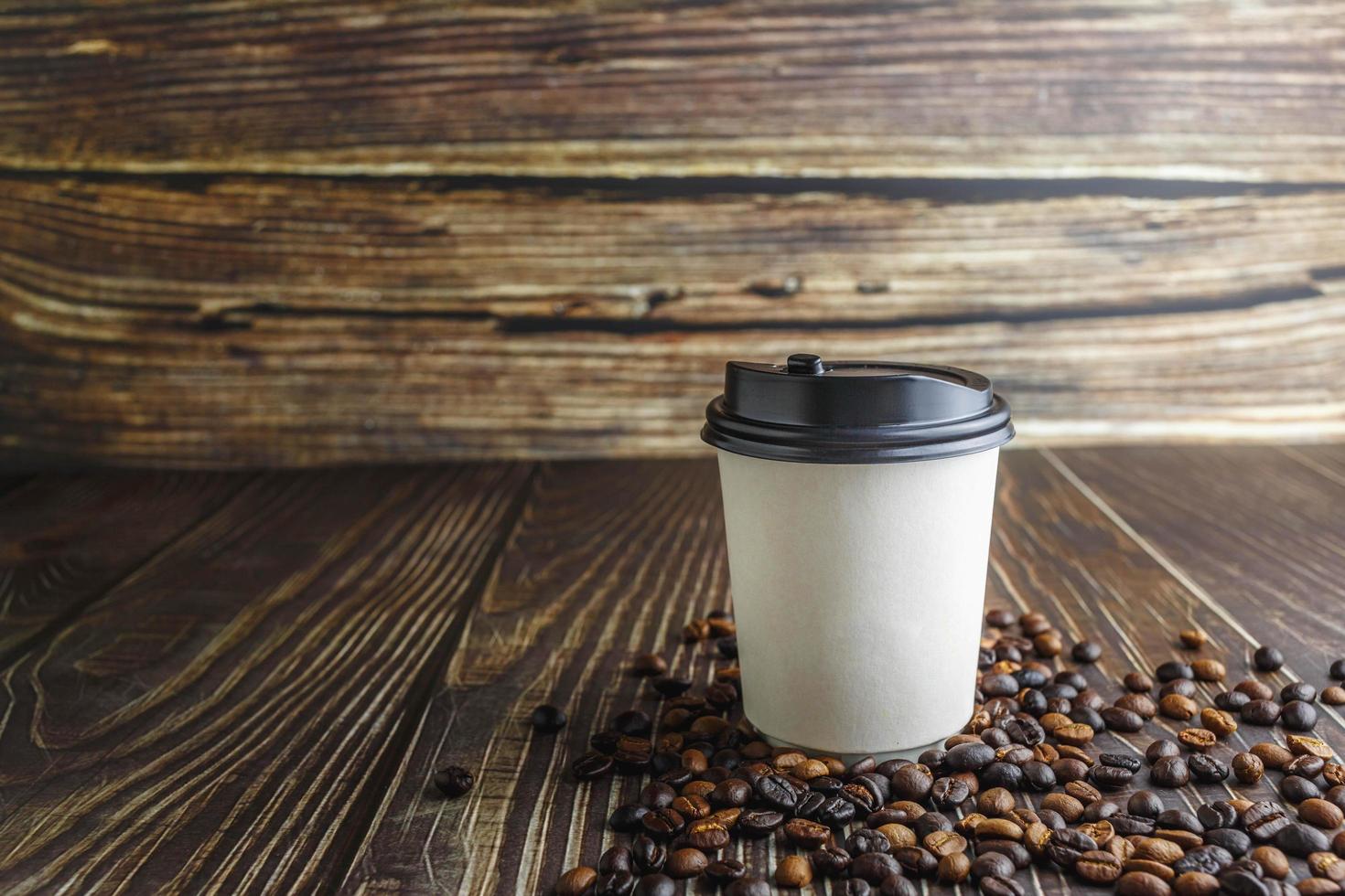 Paper coffee cup with coffee beans on wooden table photo