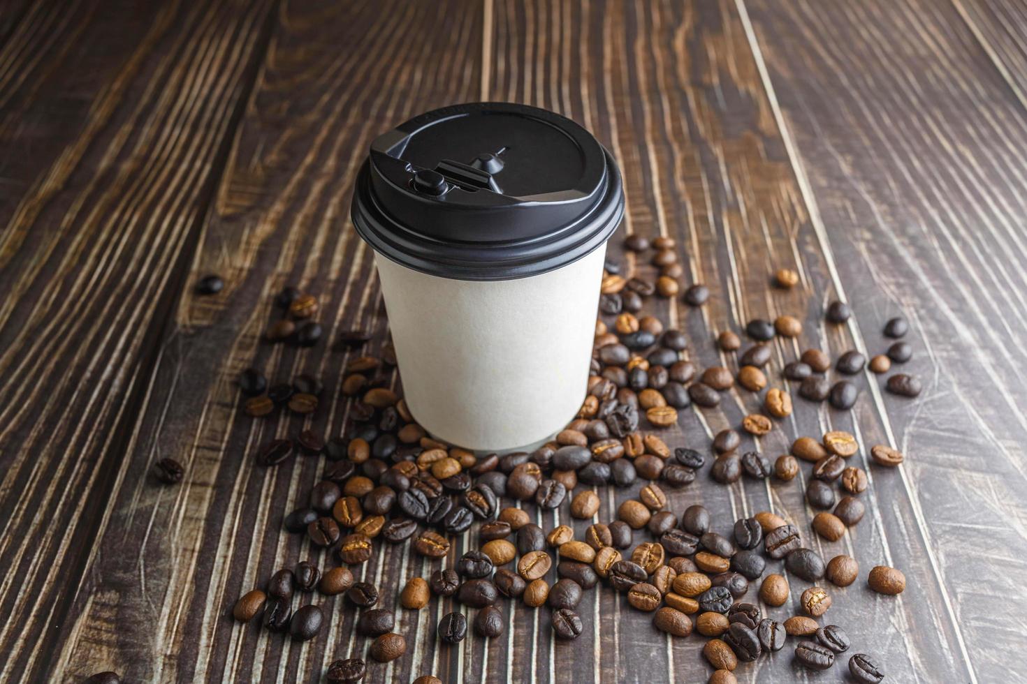 Paper coffee cup with coffee beans on wooden table photo
