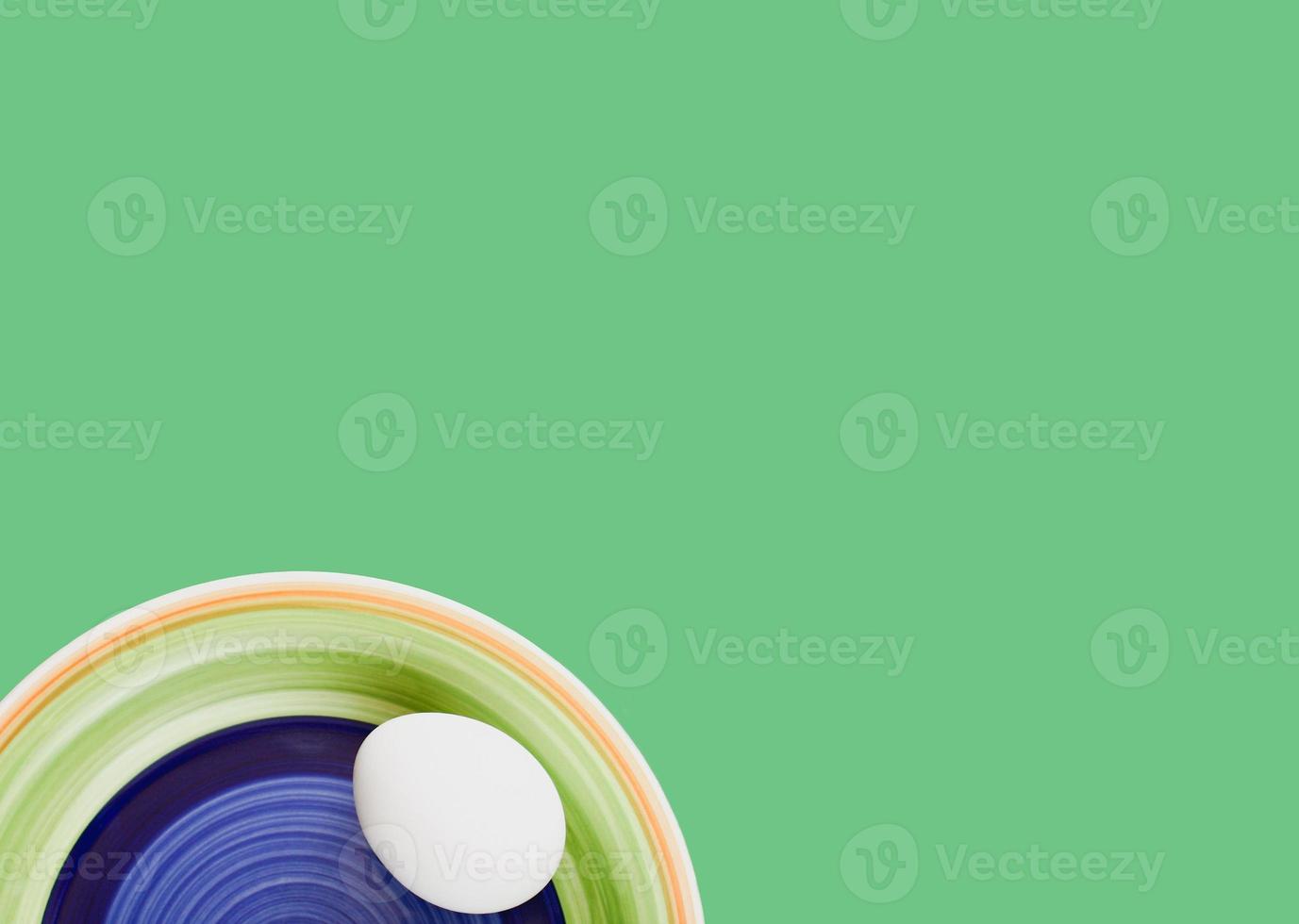 Colorful plate with a white egg isolated on green background. photo