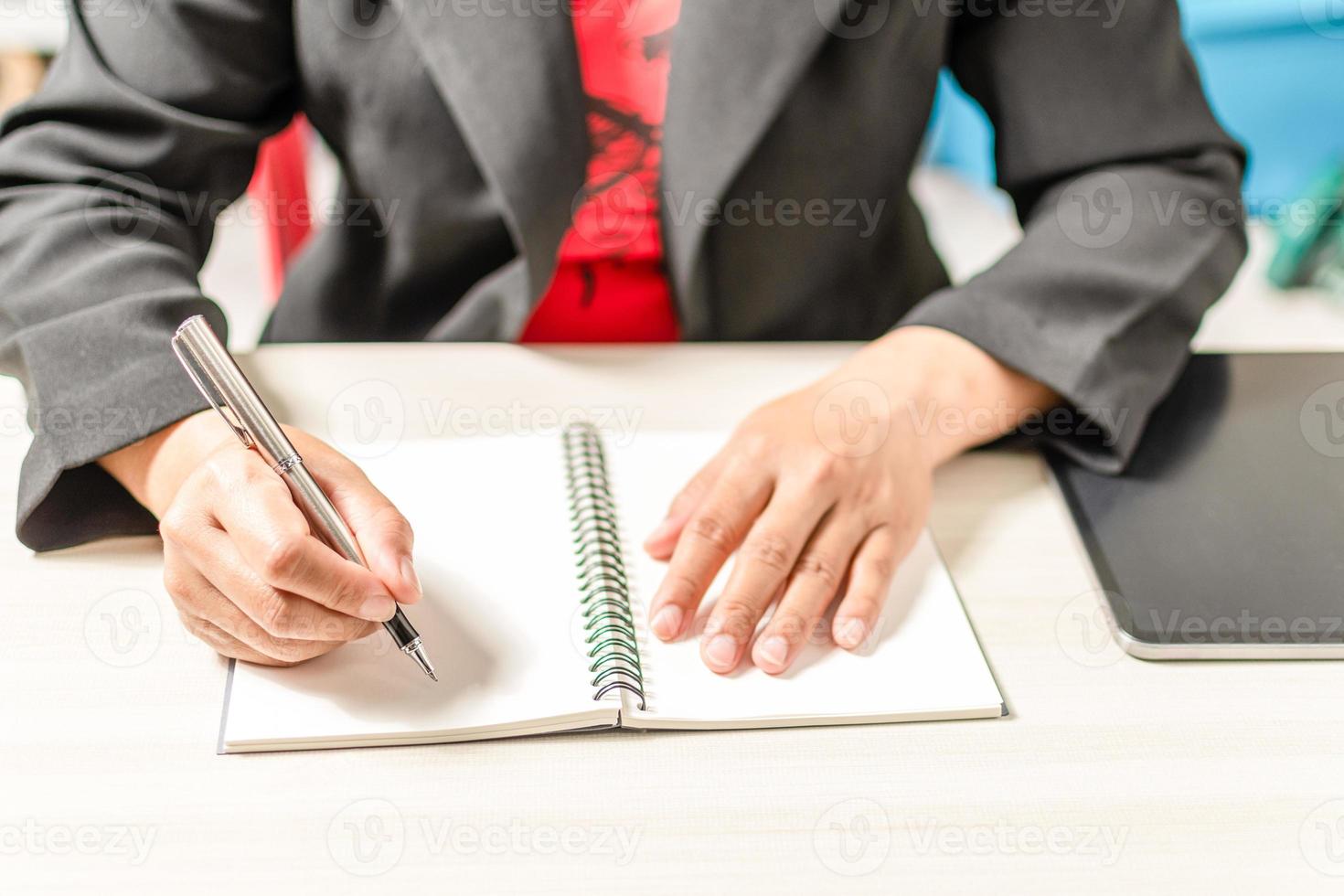 Close-up and selective focus of a woman's handwriting with a notebook placed on a wooden desktop. Concept businesswoman is keeping a record of planning marketing, investment, finance, banking, trading photo