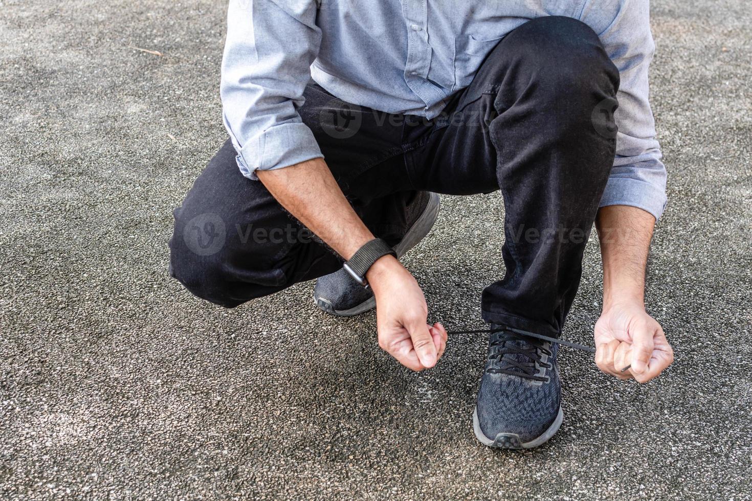 A man wears jeans tying black shoelaces in the sunlight on a sunny day in the park. selective focus, Closeup, Copy space, Blurred background photo