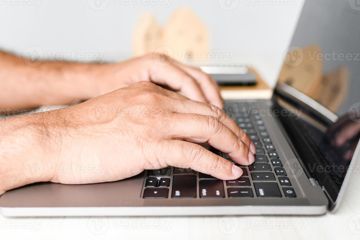 A man sits at a desk and is using a laptop computer. concept working from home, online, use of technology, online shopping, freelancing, internet. Selective focus, closeup, white blurred background. photo
