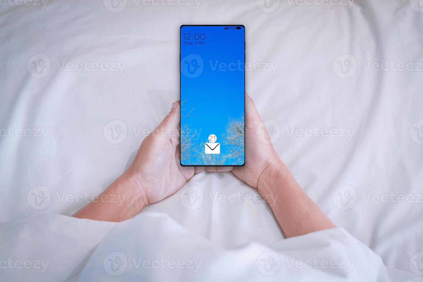 Guy holding his smartphone while waking up on the bed photo