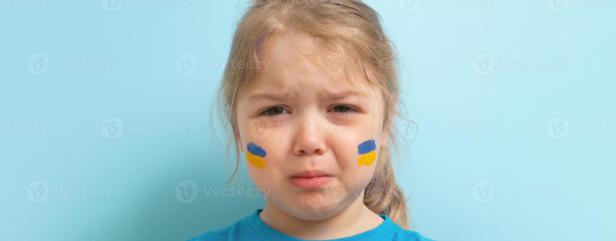 niña triste con un patrón amarillo-azul en la mejilla. bandera ucraniana y concepto de niño foto