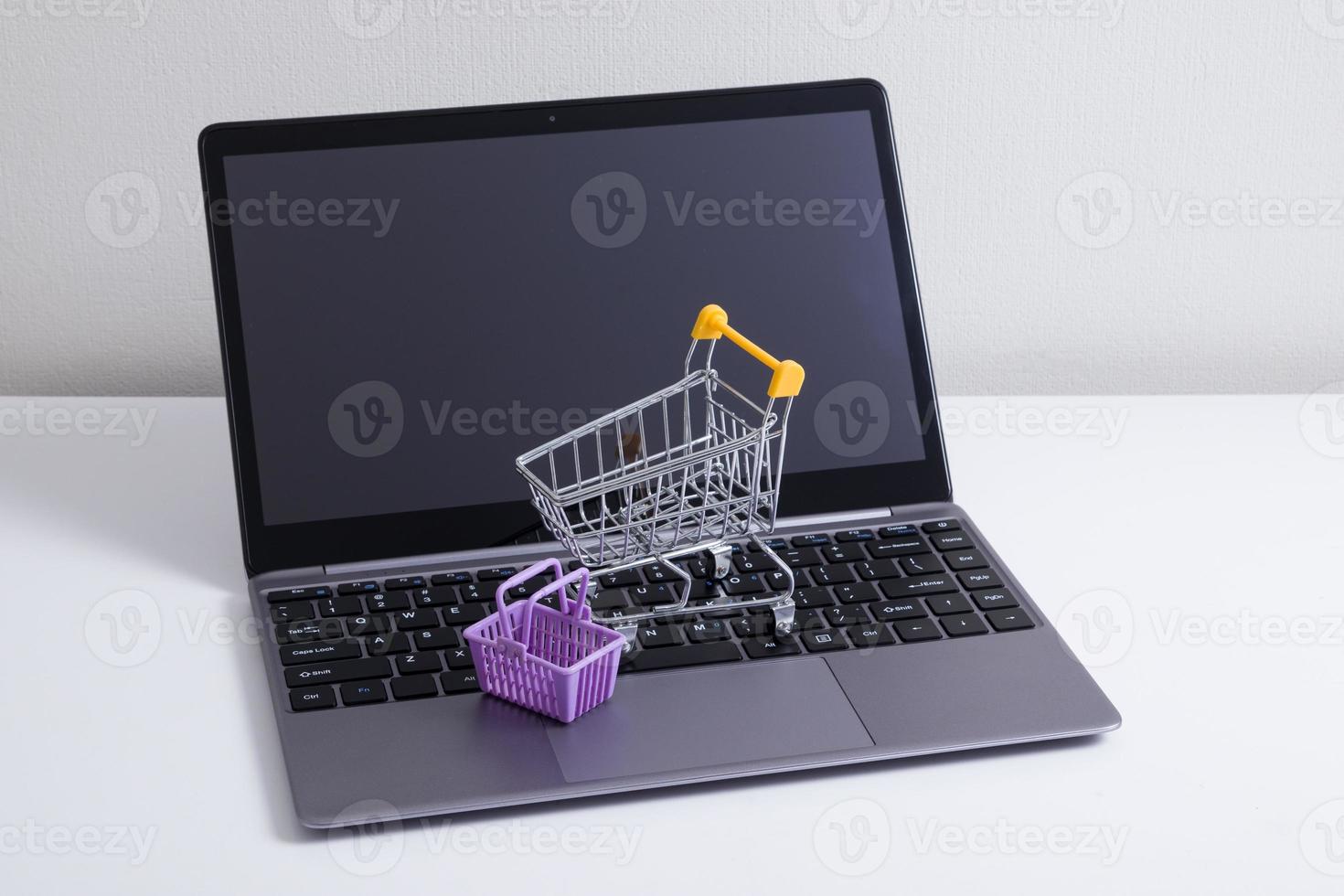 Open laptop with supermarket trolley and basket on the table. Online shopping from home photo