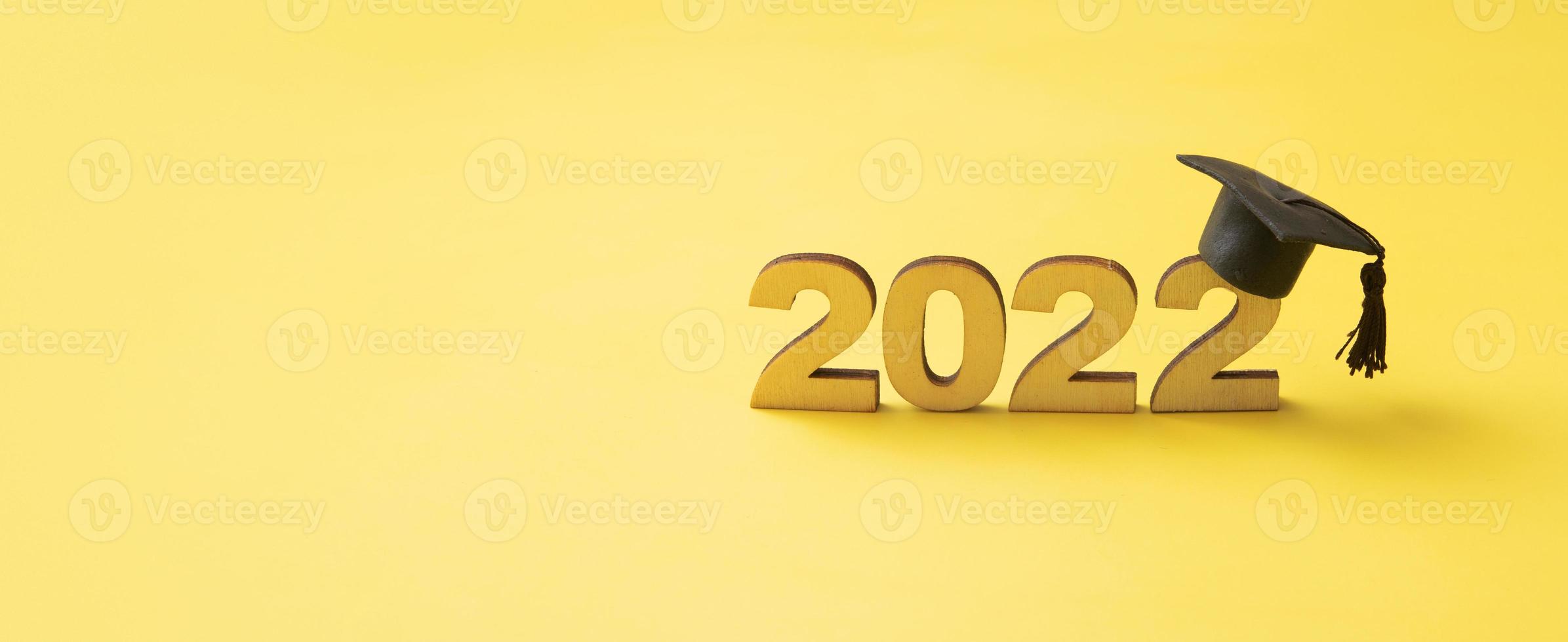 sombrero o gorra graduados con el número de madera 2022 sobre un fondo de brillo amarillo. formato de banner de clase 2022 foto
