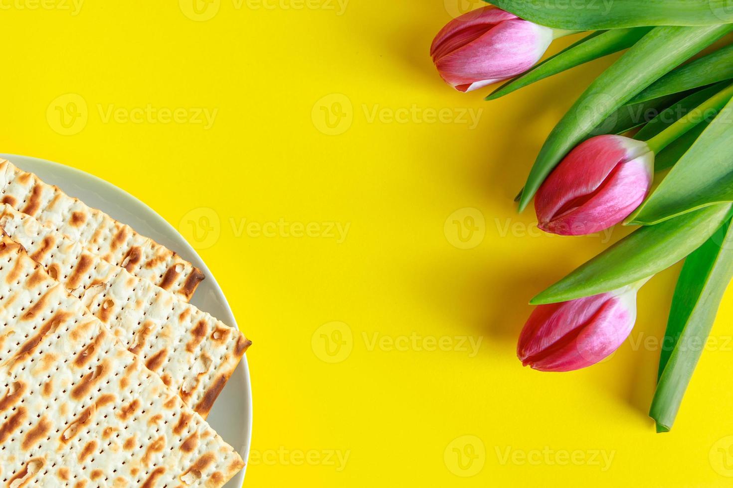 Traditional Jewish food matzo bread and pink tulips on a yellow background. Happy Passover. Religious spring holiday Pesach. Copy space. photo