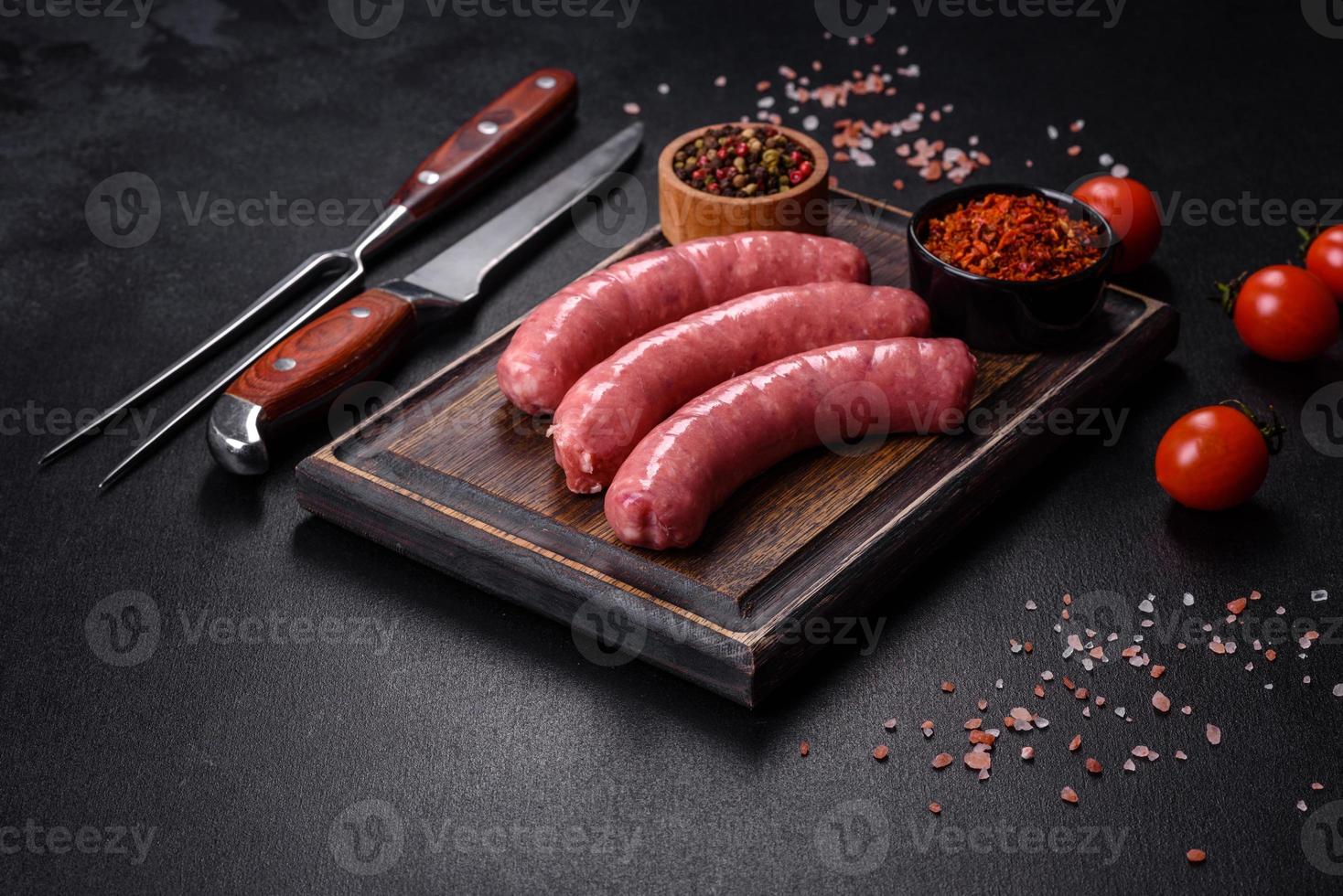 Raw sausages with ingredients on a cutting board on a stone background with copy space photo
